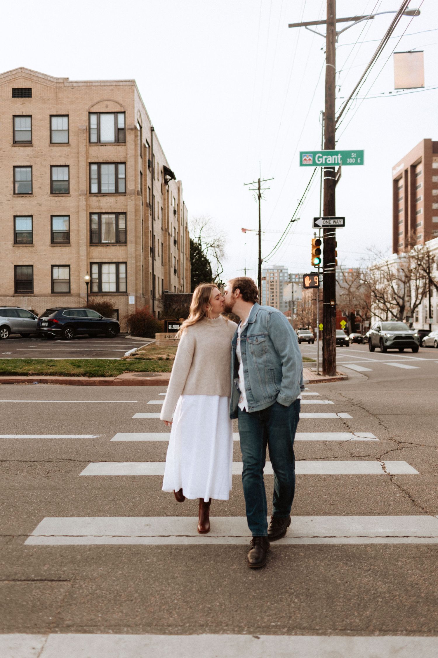 Romantic couple walking across a city crosswalk in casual attire.