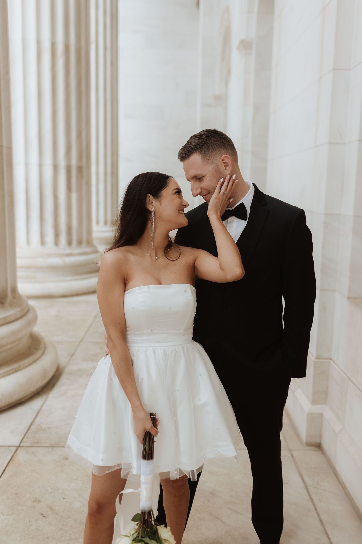 Romantic wedding couple shares intimate moments between elegant white columns.