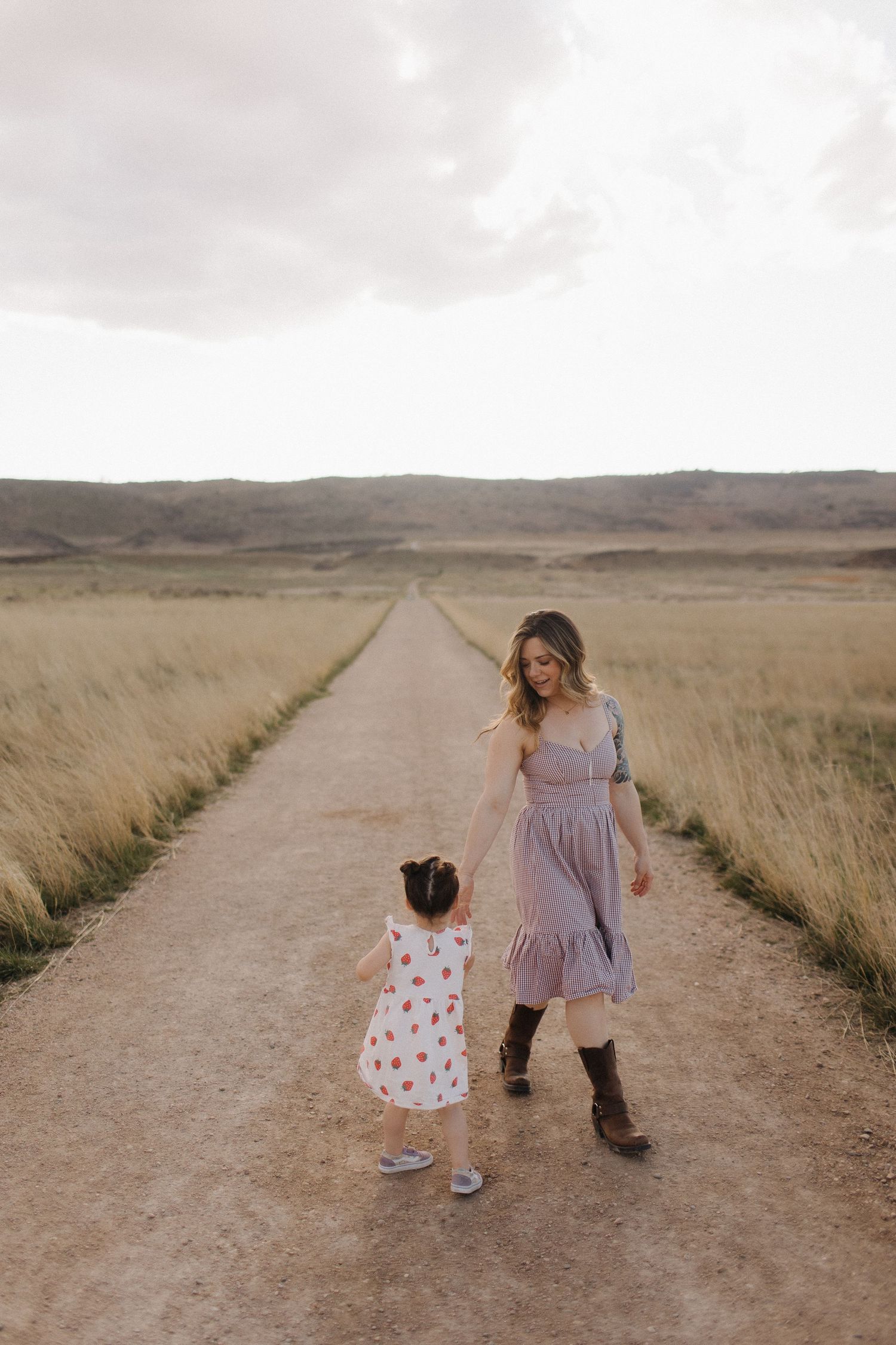 Two people walking hand in hand down a dirt path through golden fields.