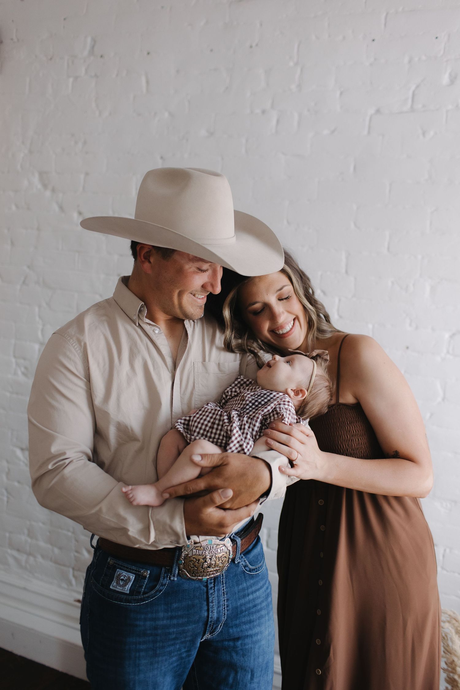 Family sharing intimate moments against a white brick wall background.