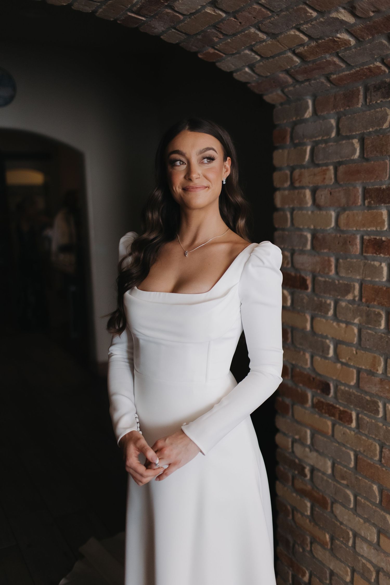 An elegant long-sleeved white wedding dress with square neckline photographed against exposed brick walls.