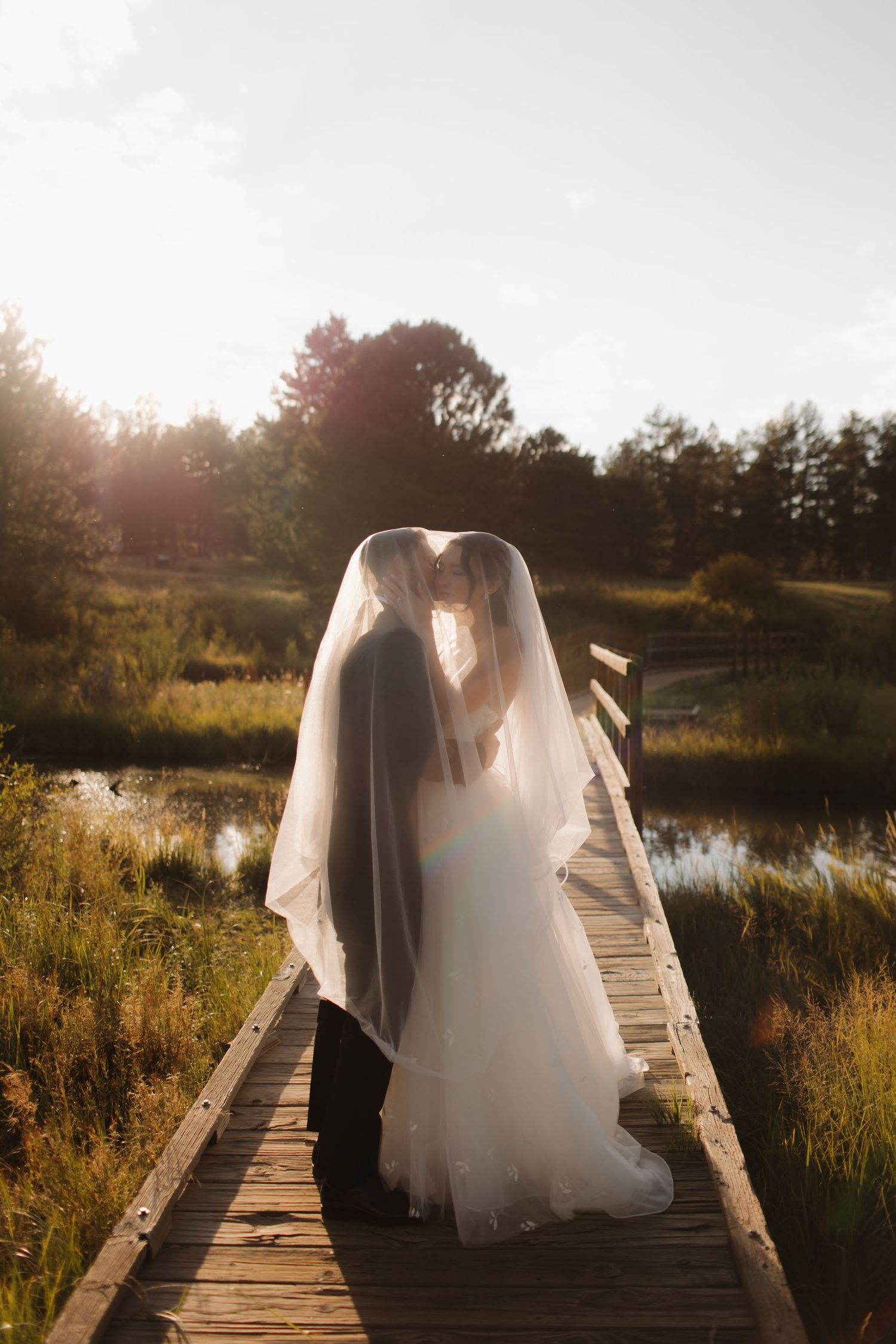 Wedding couple walking on a wooden boardwalk during golden hour with sunlit dress flowing.