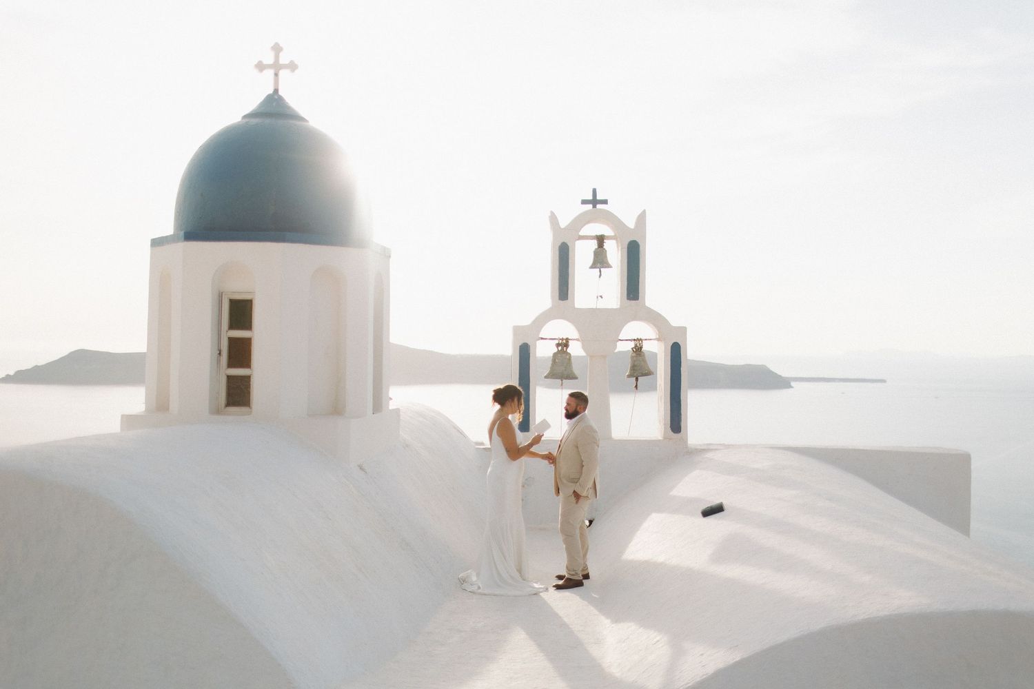Romantic wedding photos taken on a white church rooftop in Santorini with blue domes.