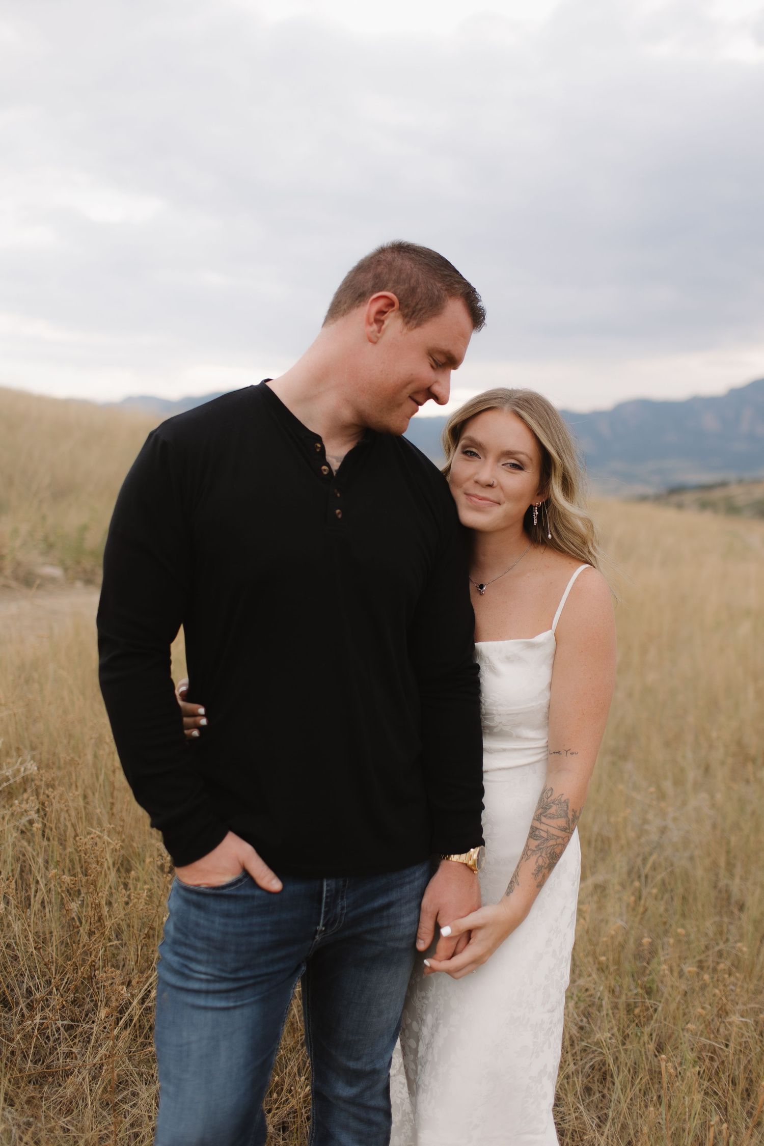 Couple sharing playful moments in field with mountain backdrop.