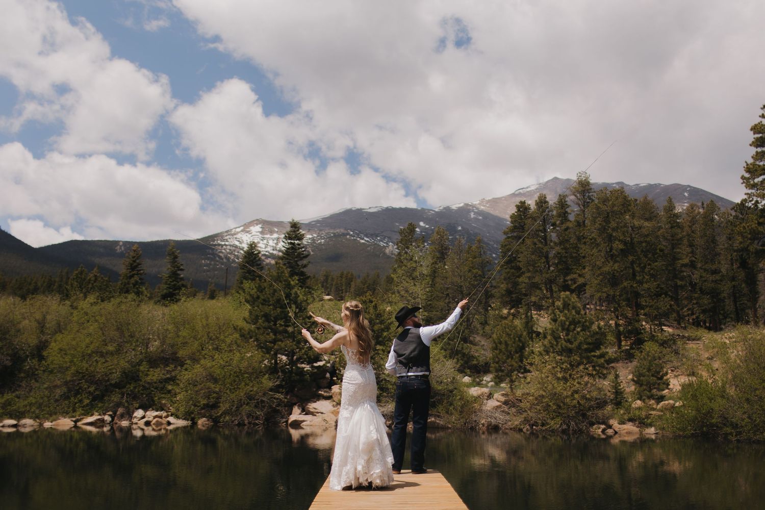 Wedding couple celebrates on a mountaintop with dramatic cloudy sky and mountain landscape in the background.