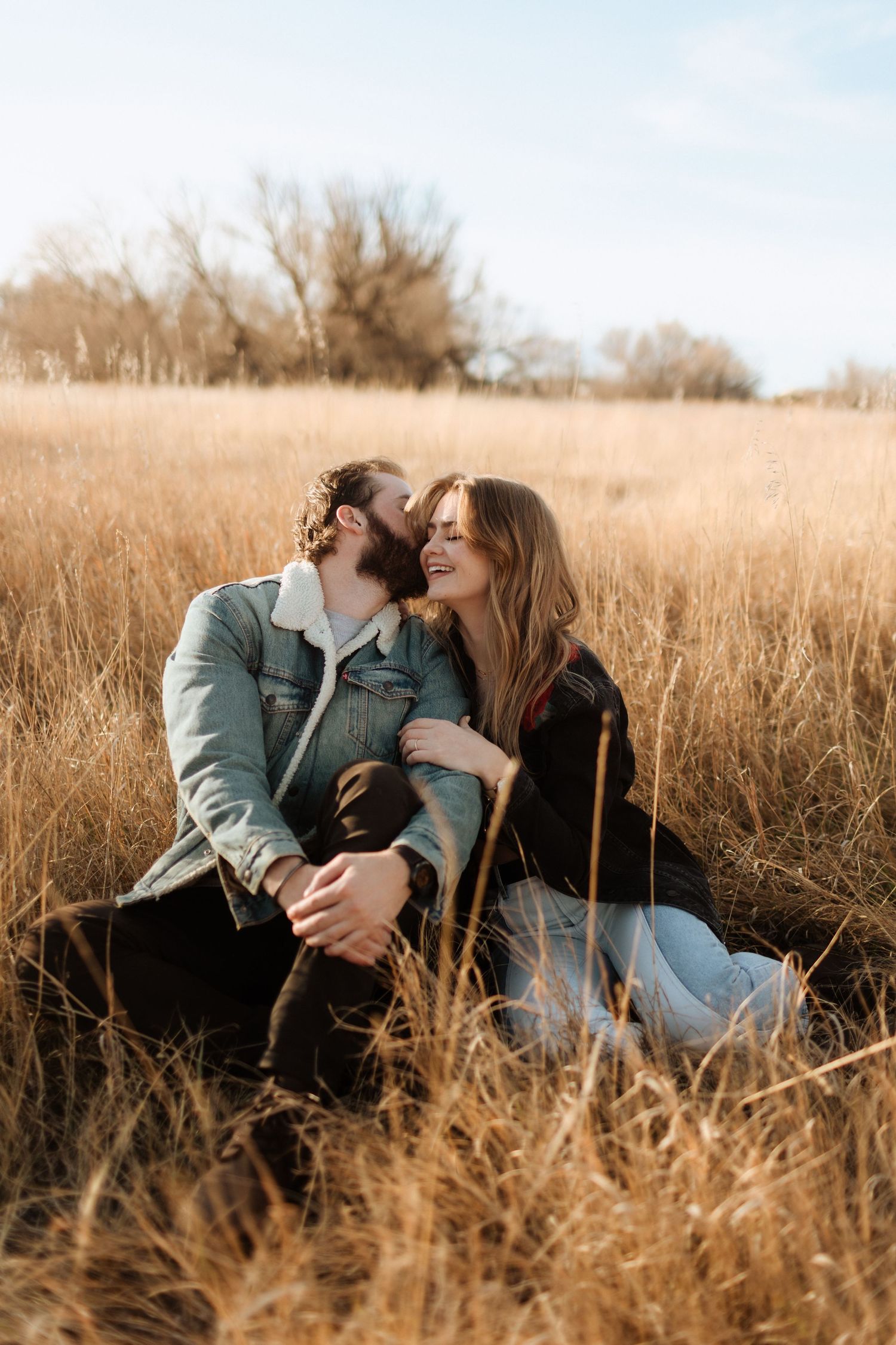 A couple shares tender moments while sitting in dried autumn grass.