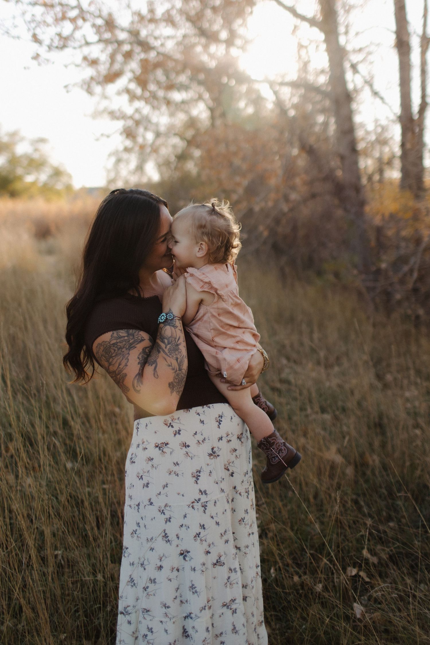 Mother and child sharing tender moments in a sunlit field with tall grass.