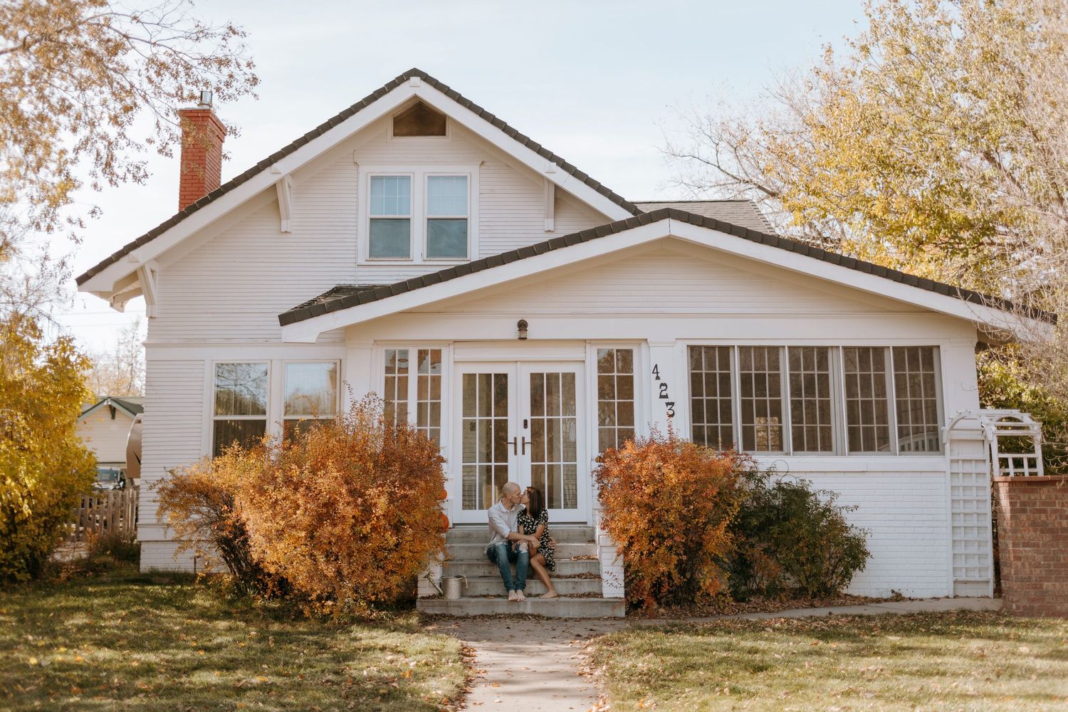 White craftsman style house with autumn trees and classic architectural details.