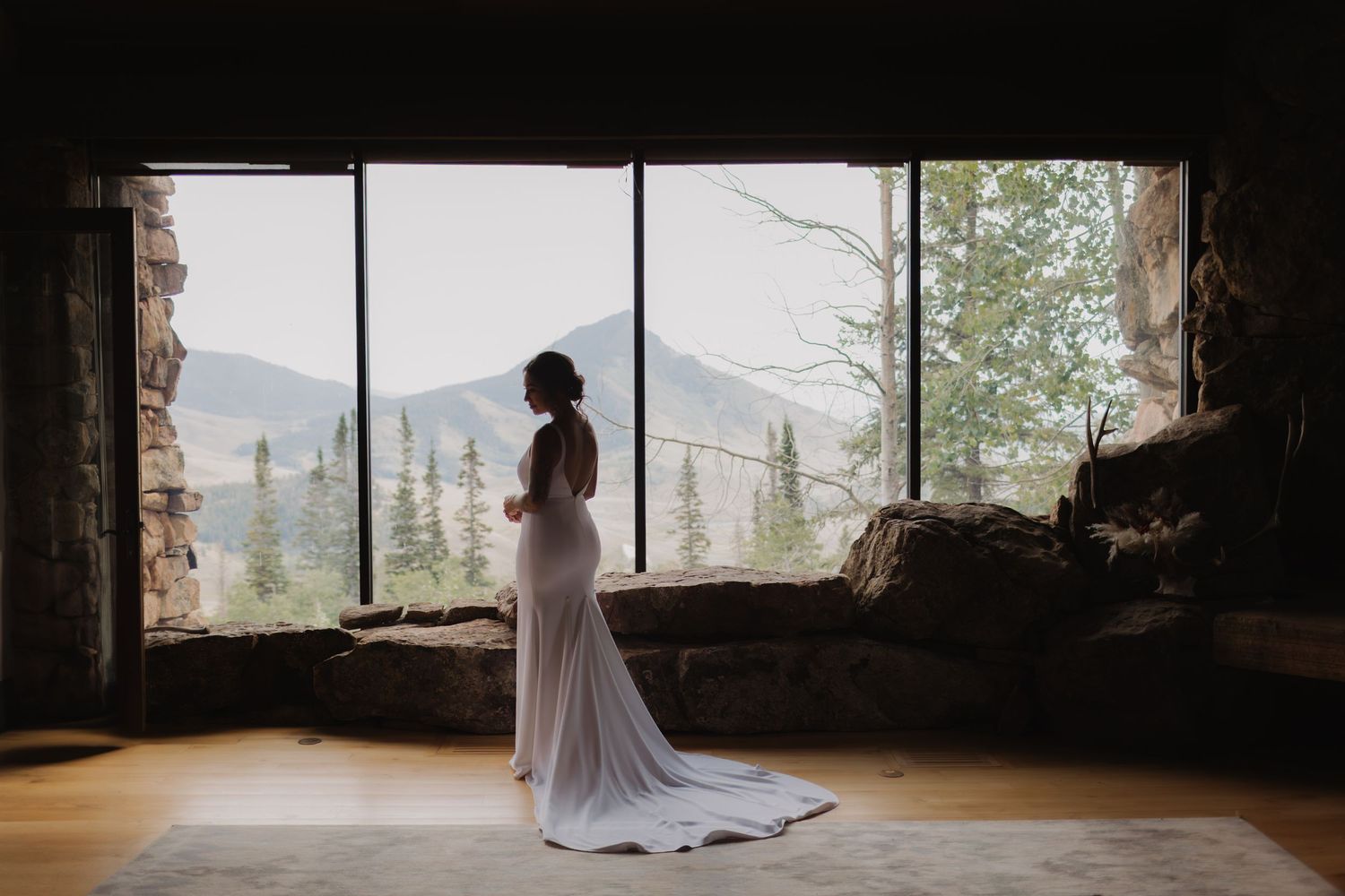 A silhouette stands in a stone window frame overlooking a mountain landscape.