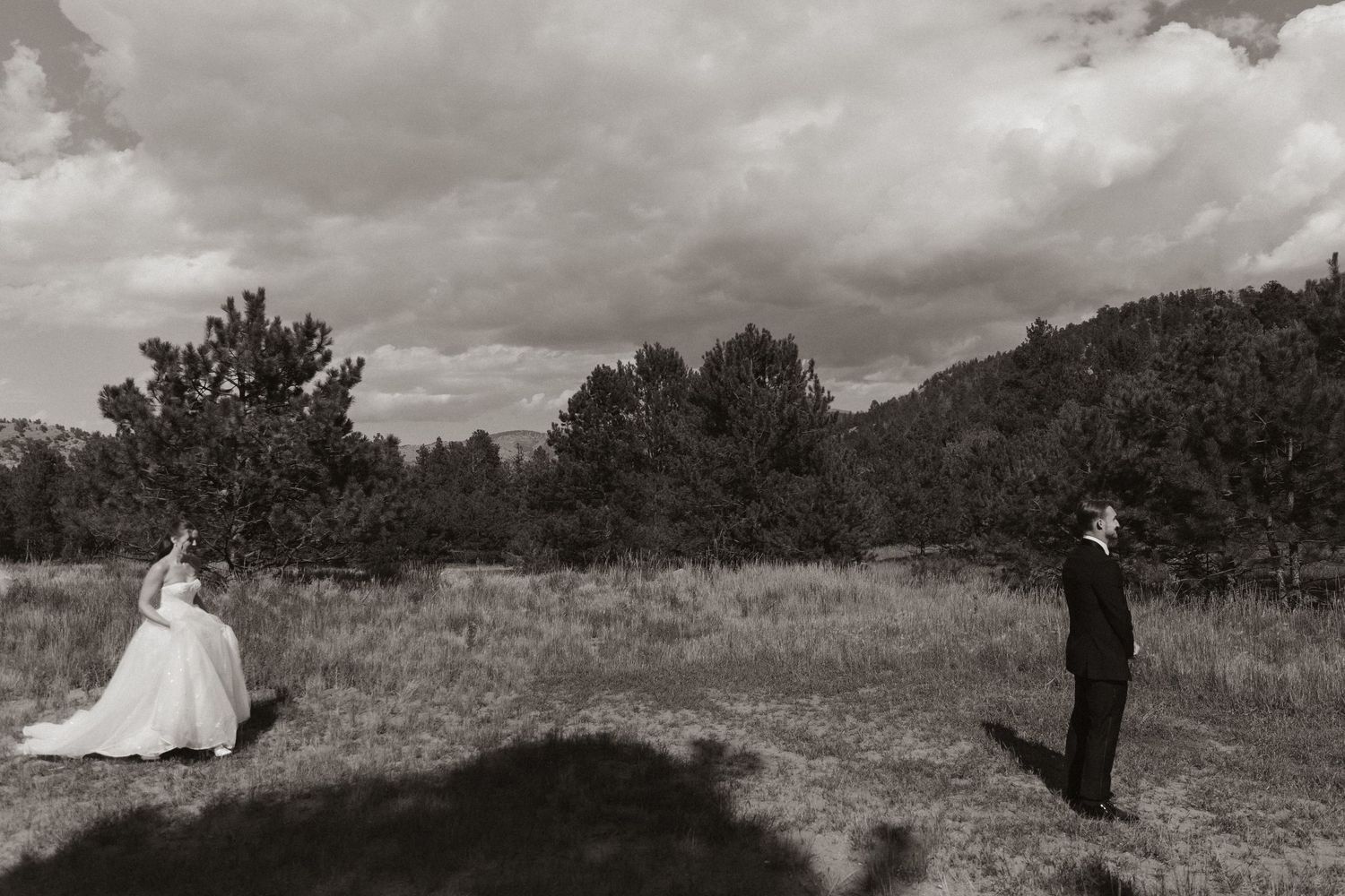 A couple in wedding attire walking together across a scenic outdoor landscape.