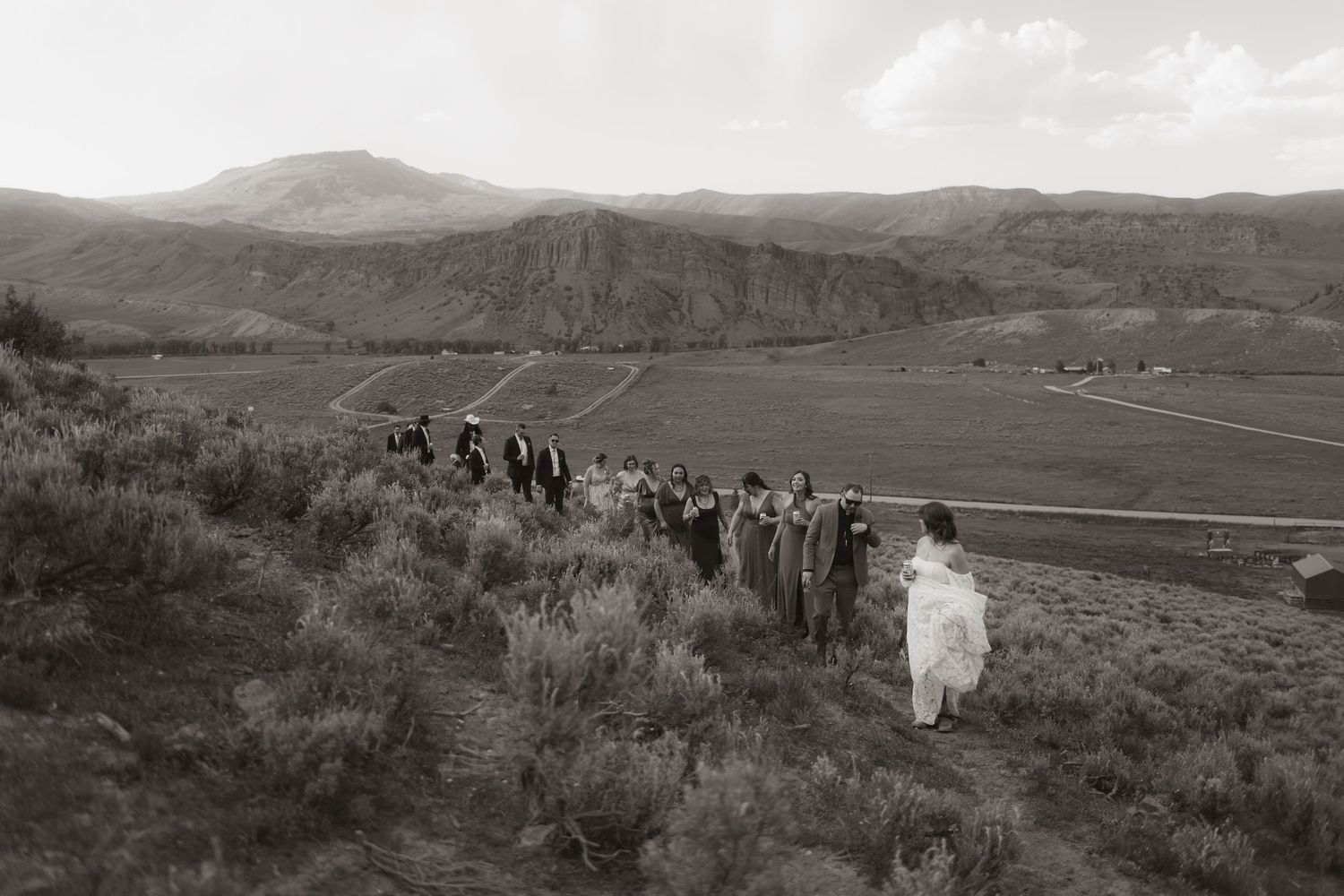 A wedding party walks along a hillside path in black and white photography.