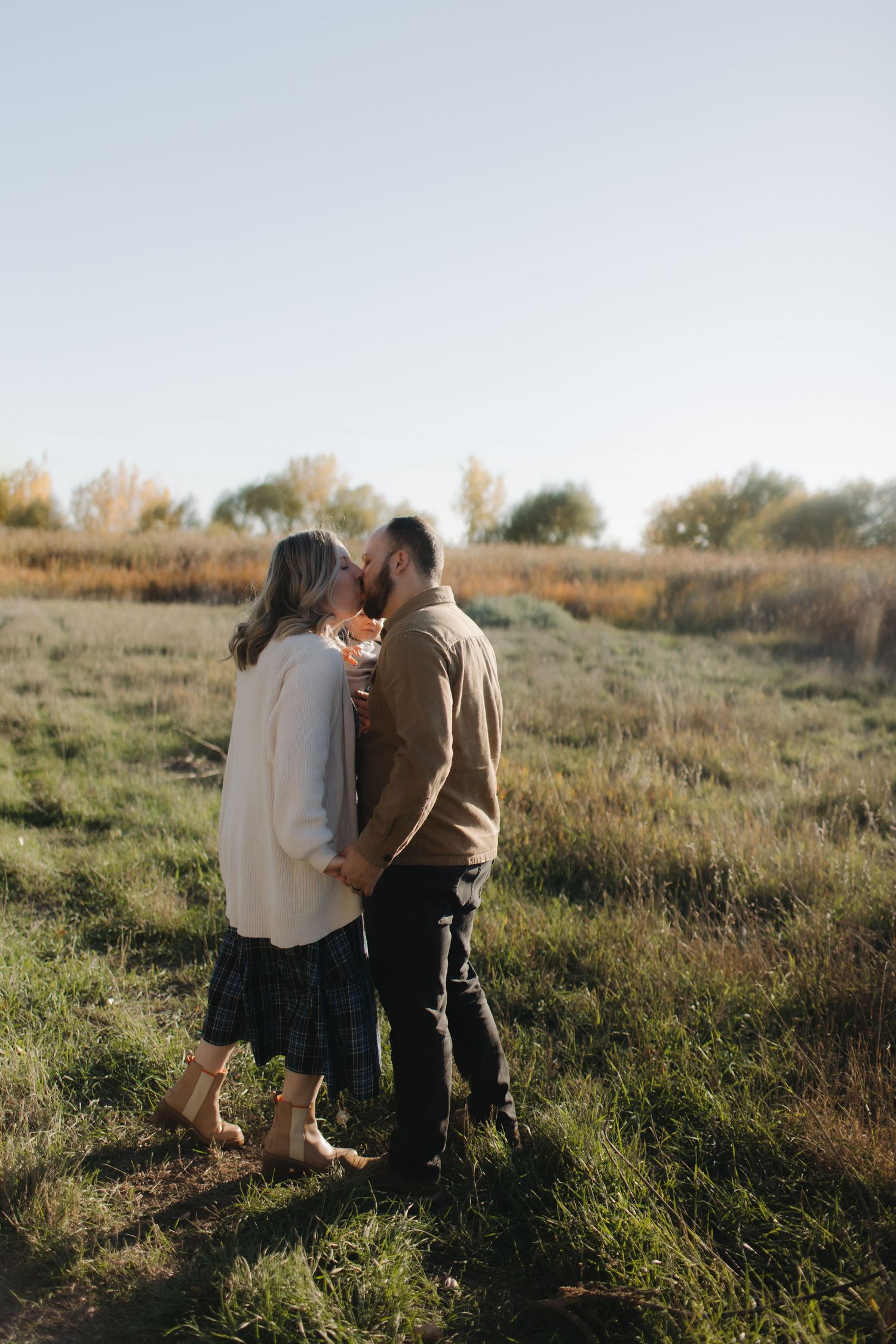 A couple shares a tender moment together in a sunlit field of tall grass during golden hour.