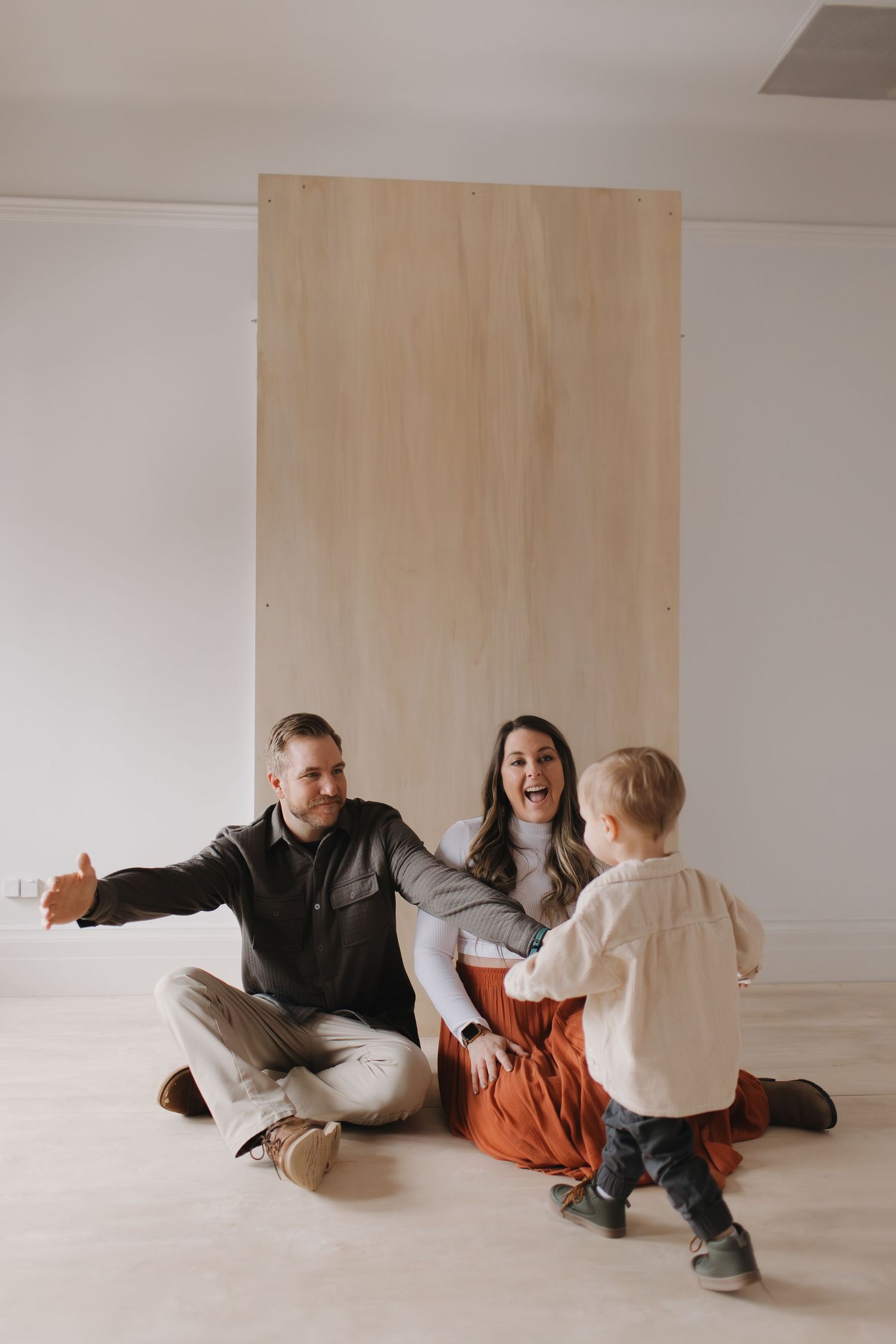 Playful indoor family photoshoot with natural light and wooden panel background.