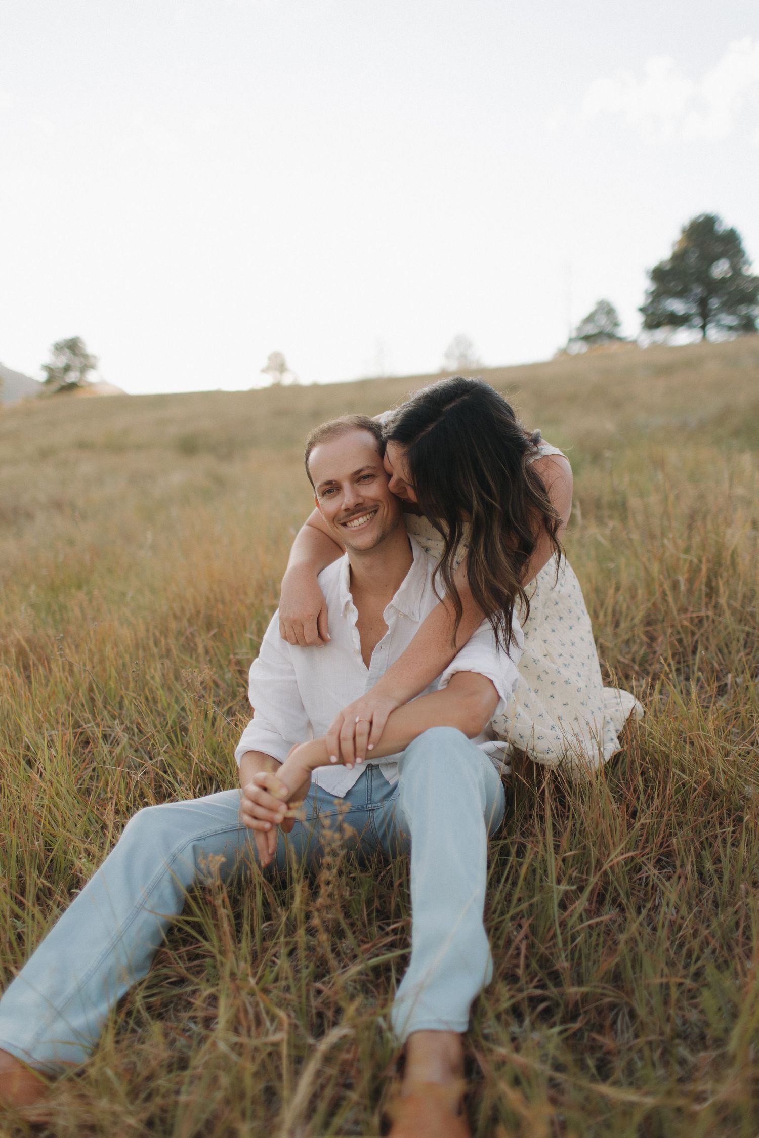 A couple shares intimate moments while sitting in tall grass during a sunset photoshoot.