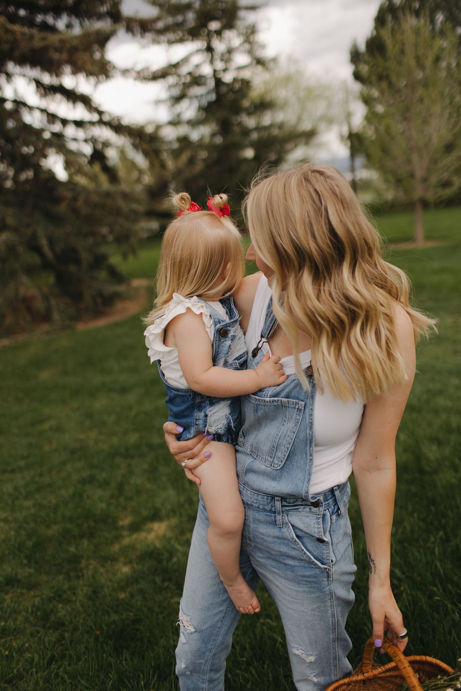 Sweet moment between parent and child in overalls against green park background.