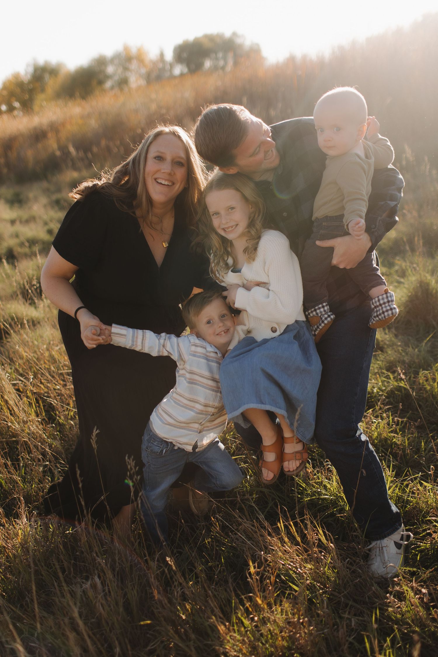 Family playing and laughing together in a golden field during sunset.