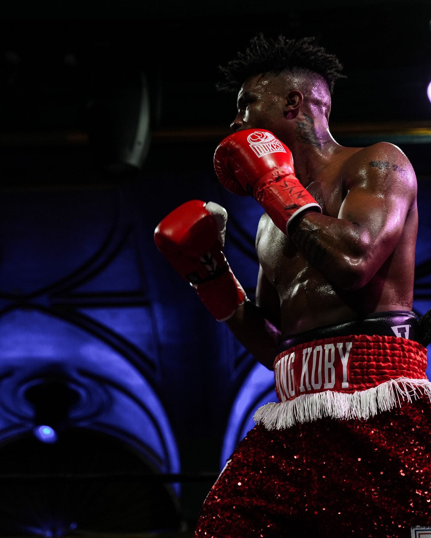 Boxer wearing red sequined trunks and gloves in dramatic lighting during a match.