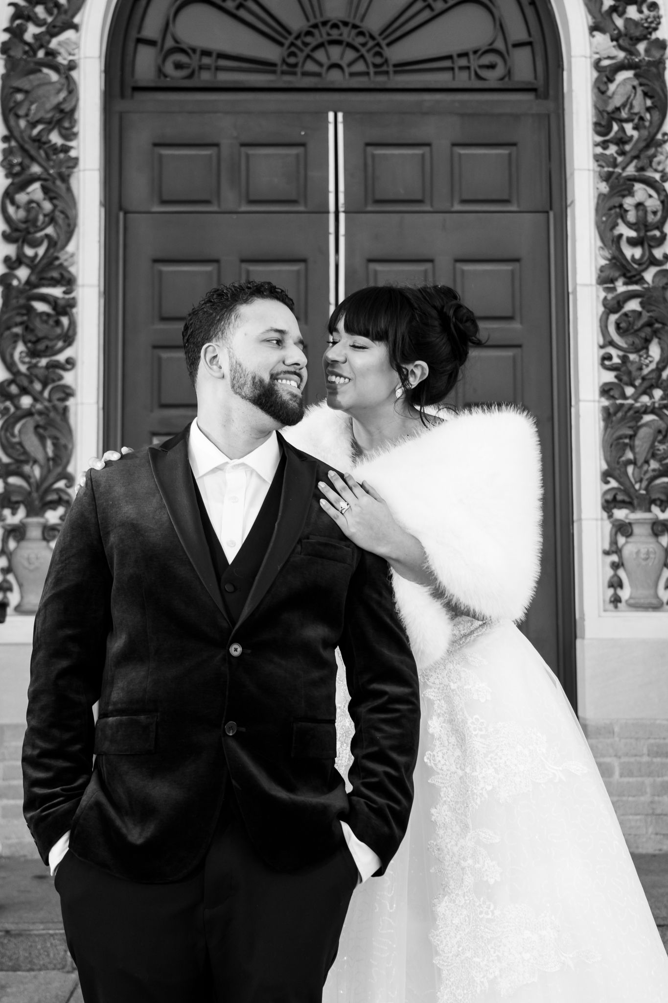 Black and white portrait of newlyweds sharing intimate moment in front of decorative doorway.