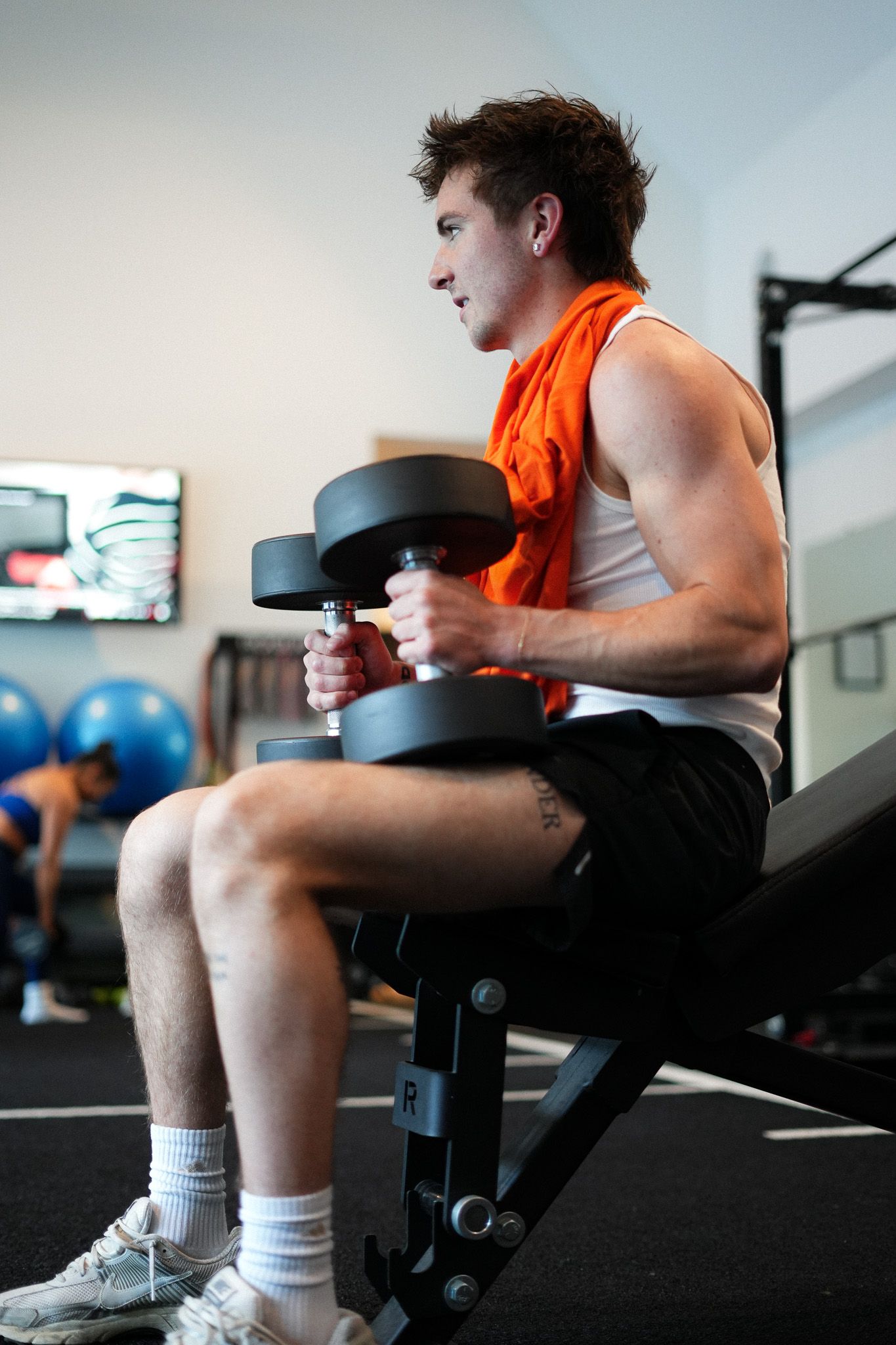 Person exercising with dumbbells while seated on workout bench in gym.