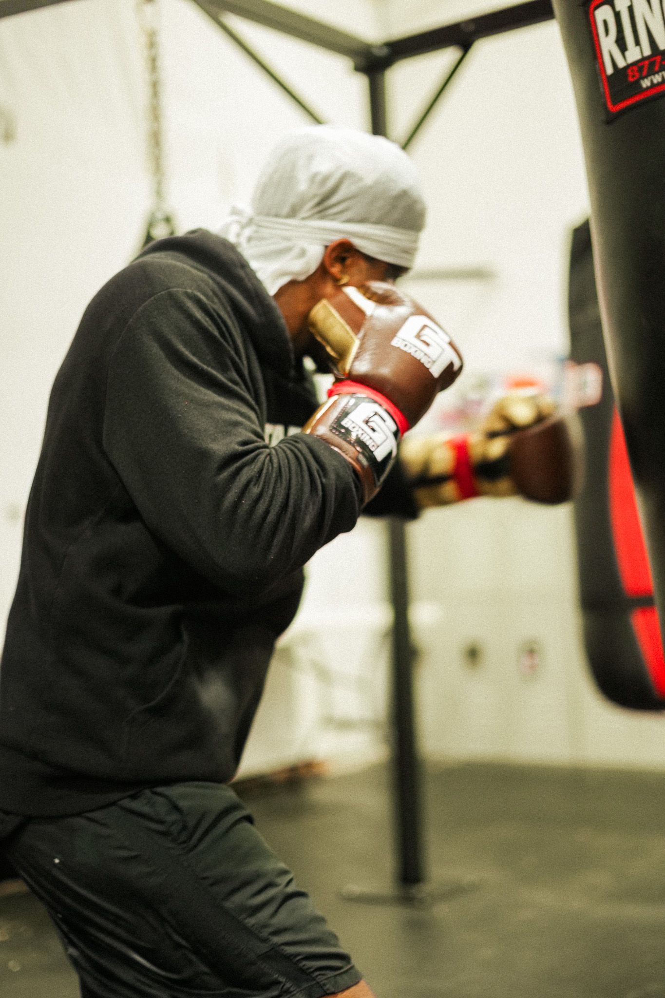Boxer in black hoodie practicing defensive moves in a dimly lit gym.