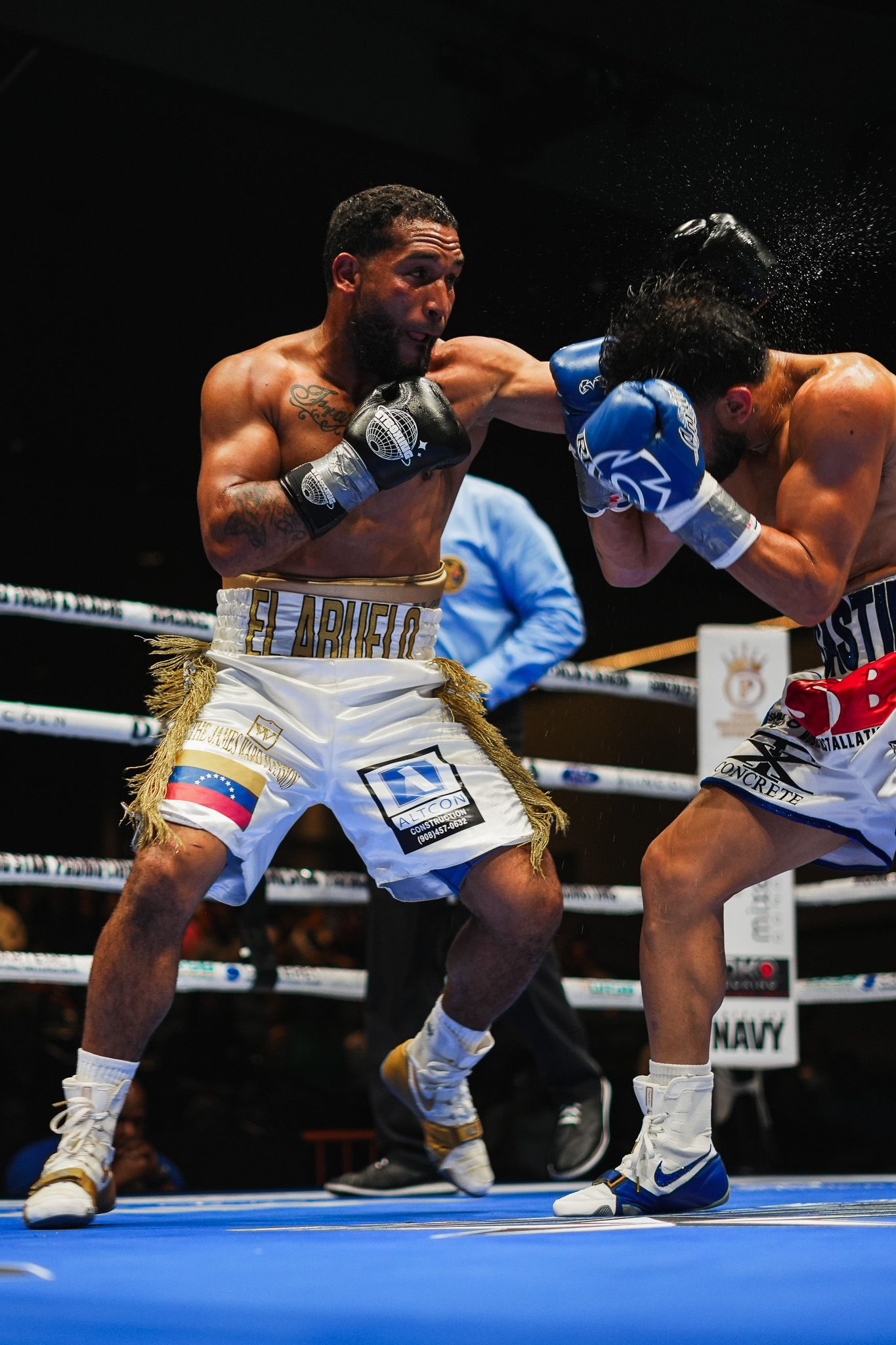 Boxers exchange low punches during intense fight action on blue canvas ring.