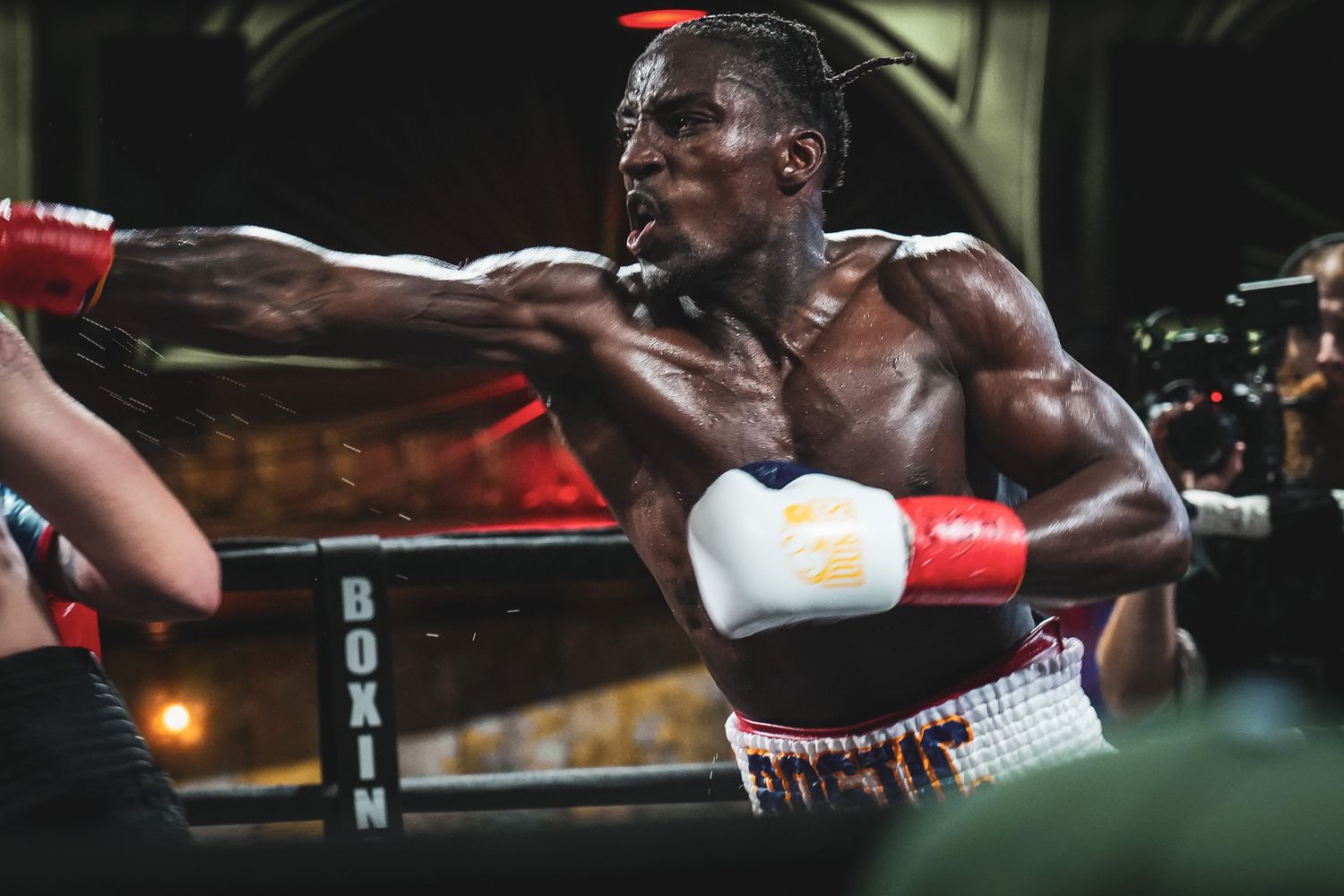Boxer throwing powerful punches during training session in dark gym environment.