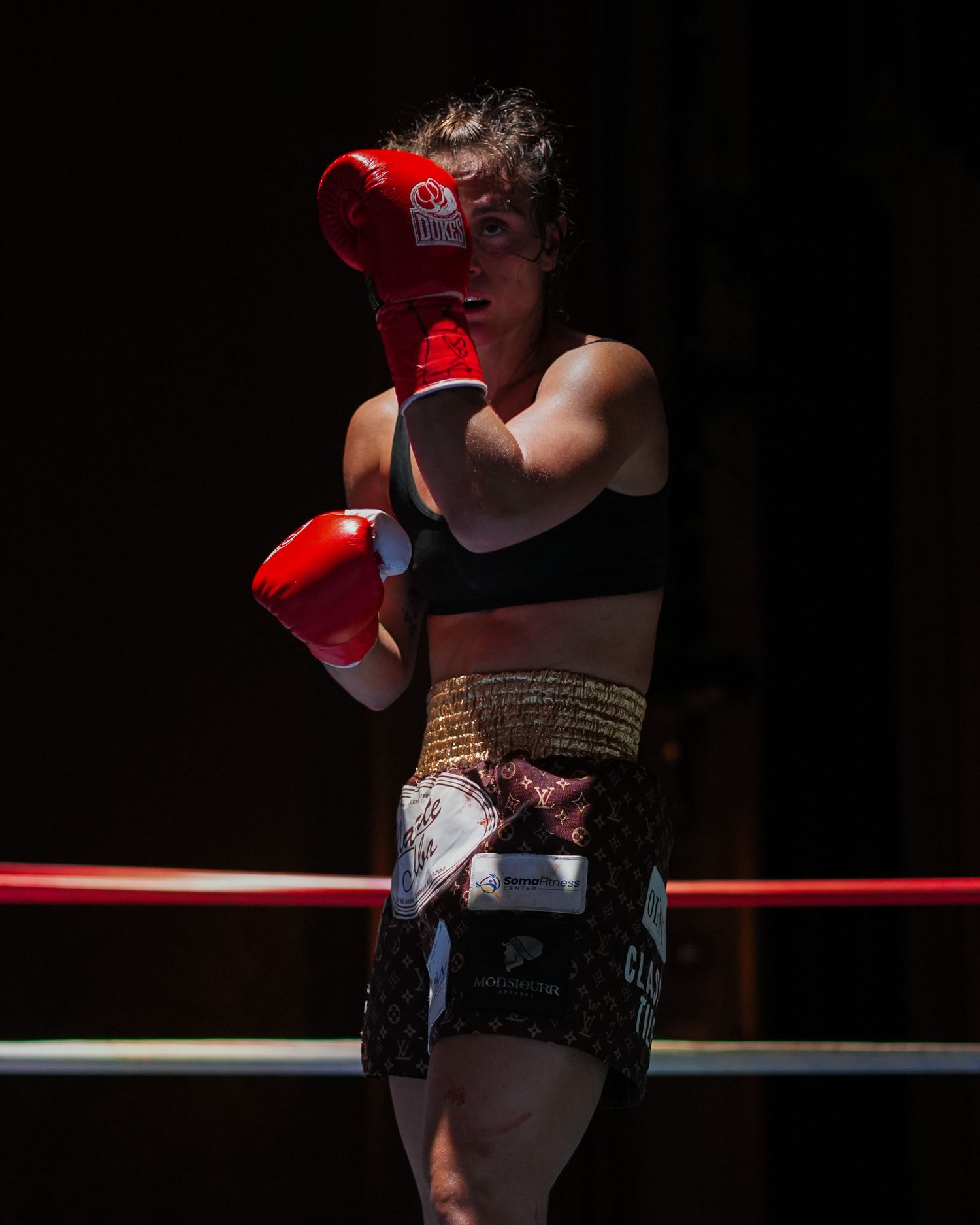 Boxer in red gloves and black sports attire poses in dramatic lighting against dark background.