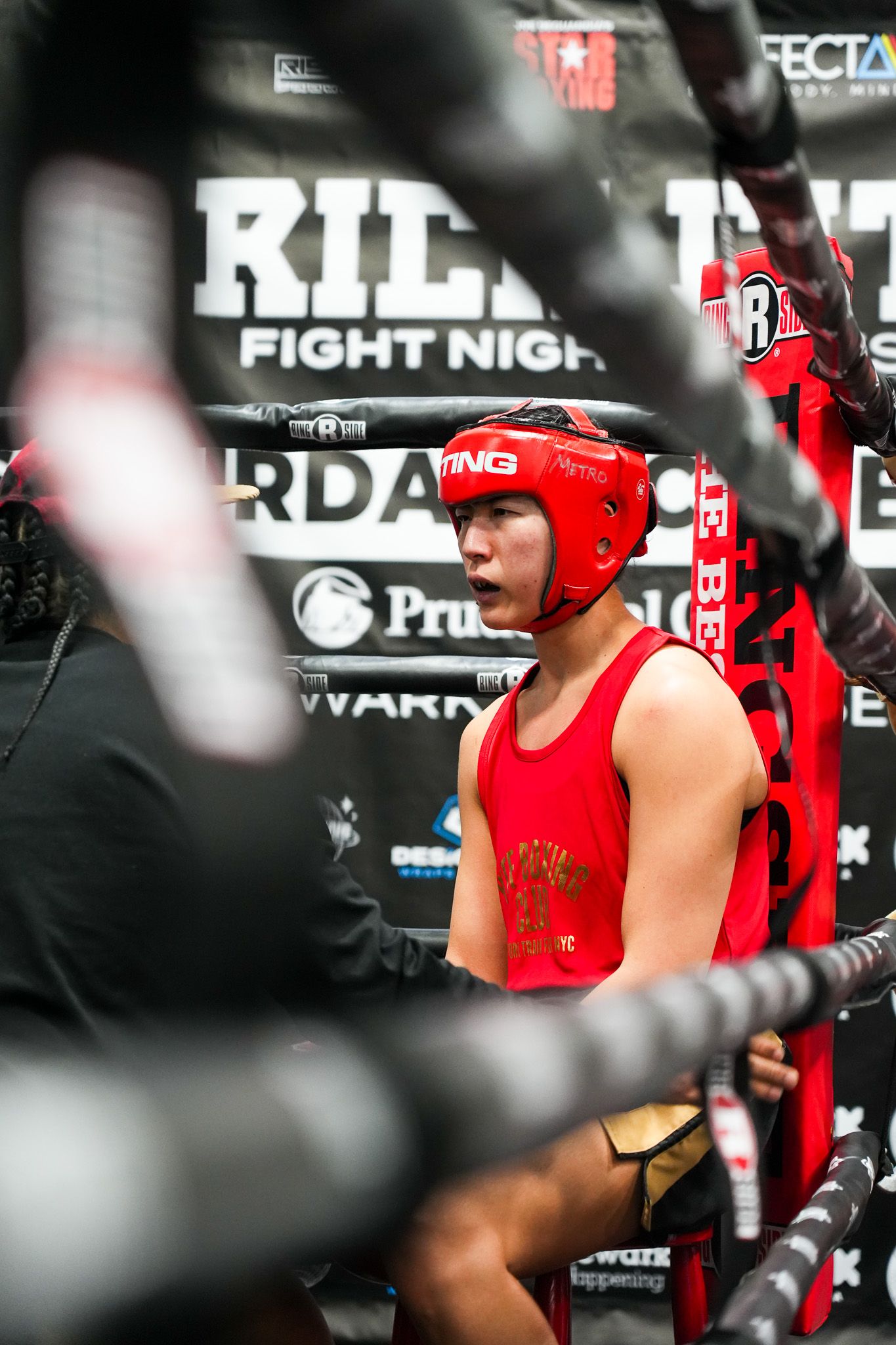 Boxer wearing red protective headgear and white shirt training in a gym ring.