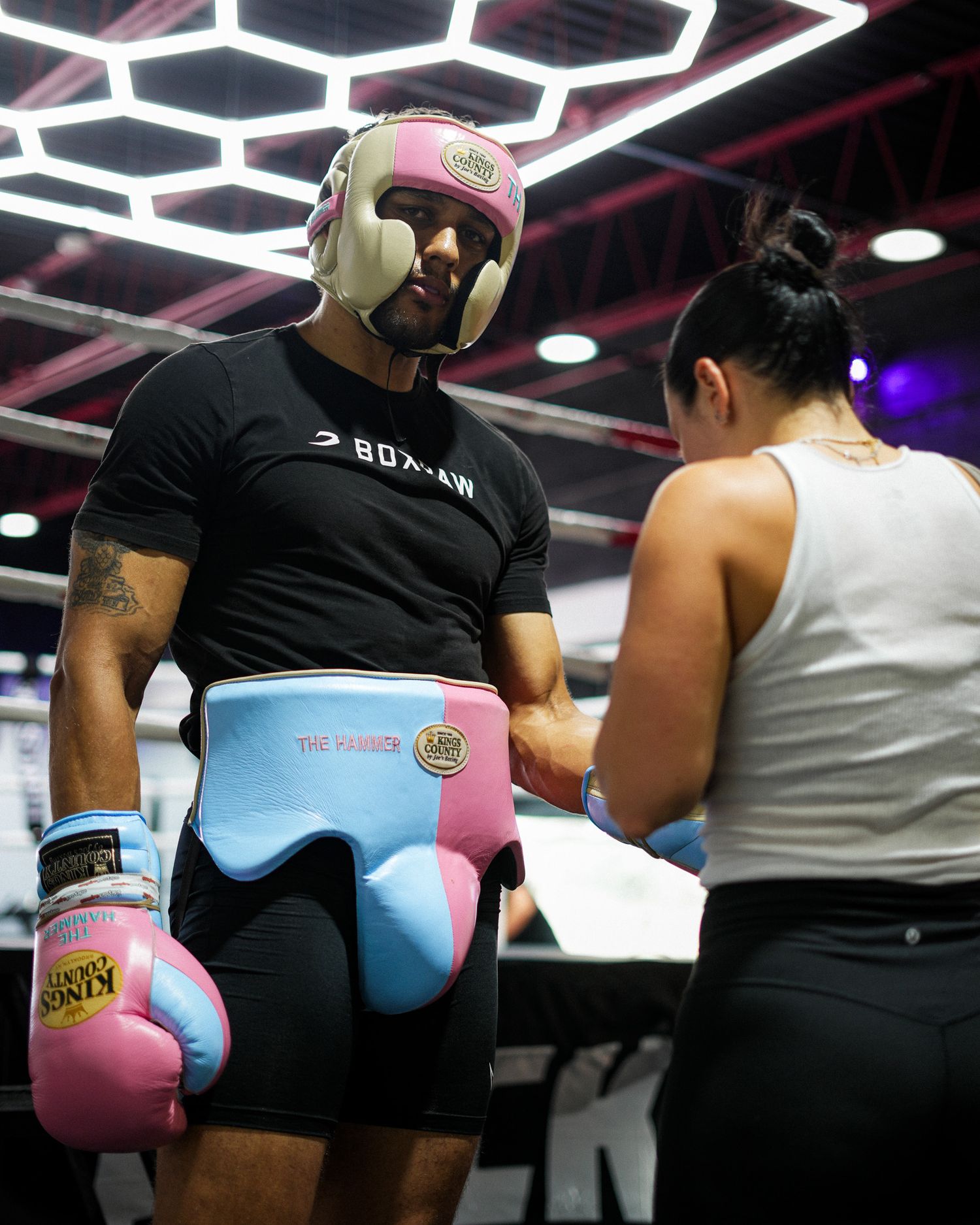 Boxer wearing protective headgear and colorful gloves stands in training gear at a boxing gym.