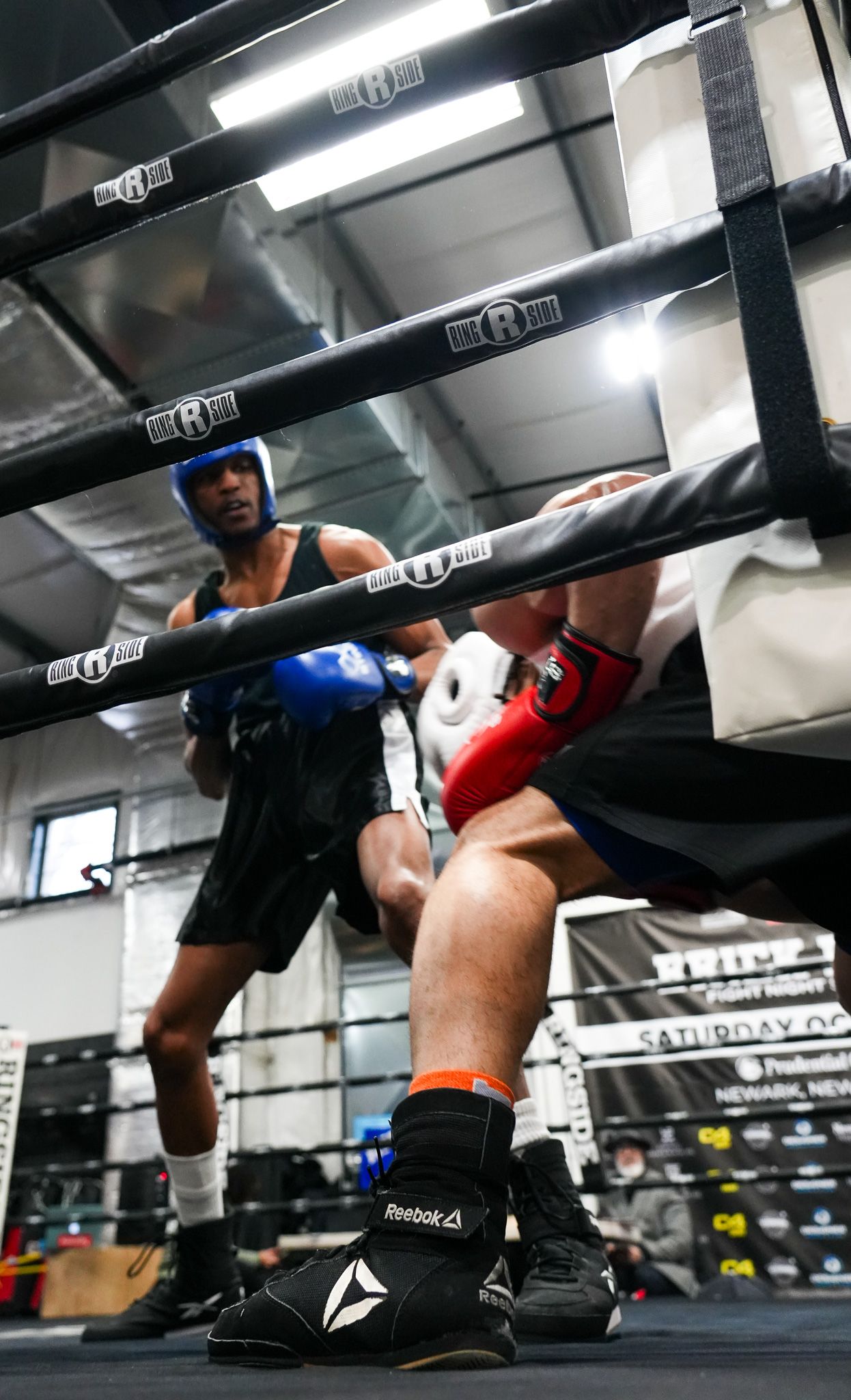 Low angle view of boxers training in a boxing ring under fluorescent lights.
