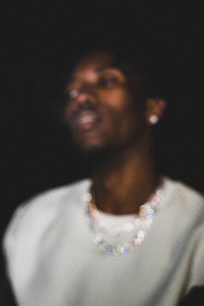 Figure wearing white sweater and crystal necklace in dark setting.