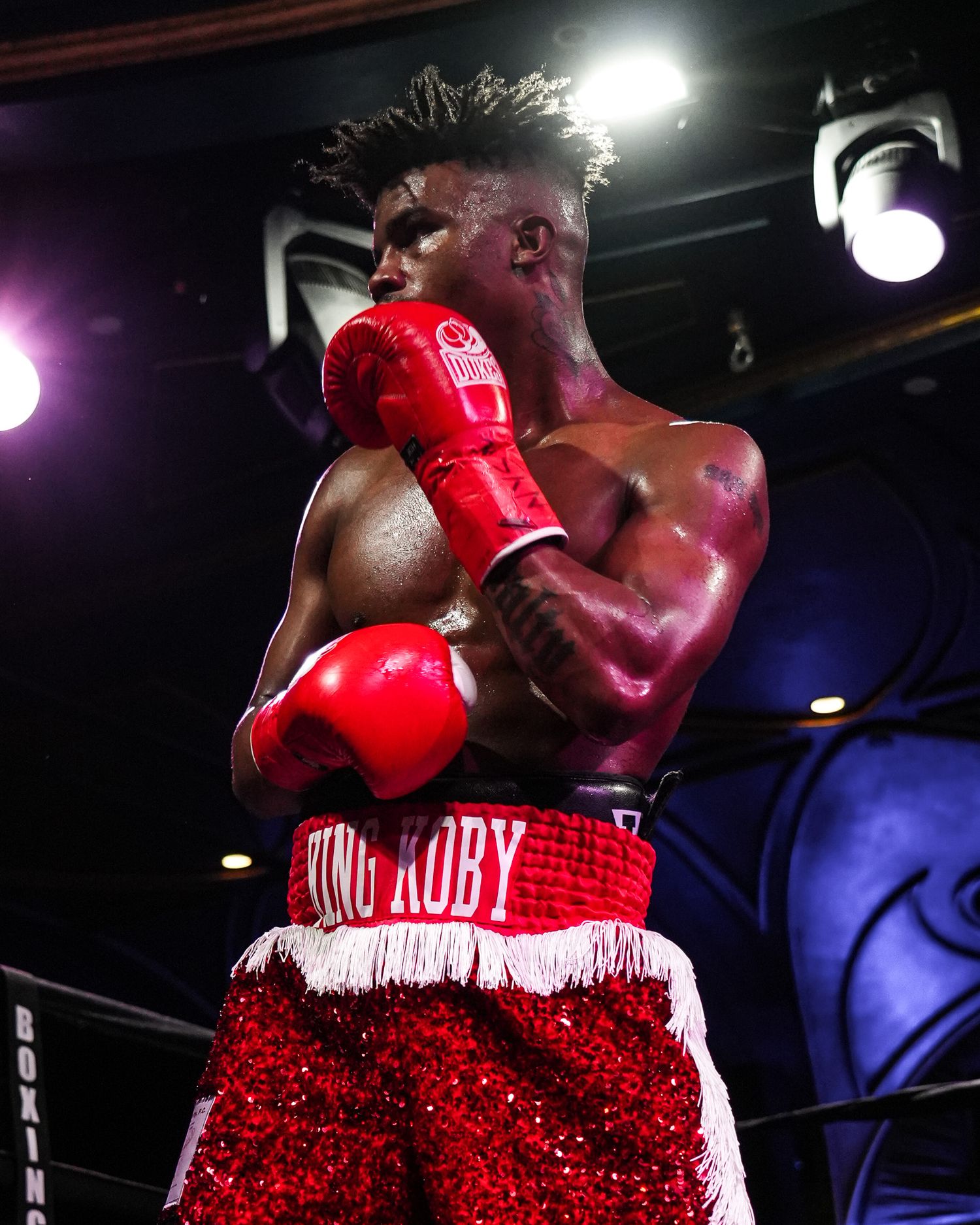 Boxer in sparkling red trunks throws a powerful punch during a night fight.