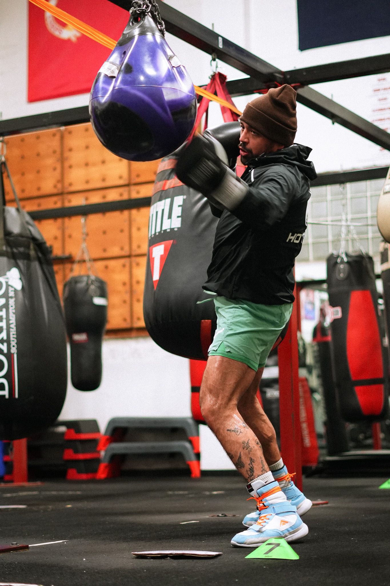 Boxer in winter gear works out with purple speed bag in training facility.