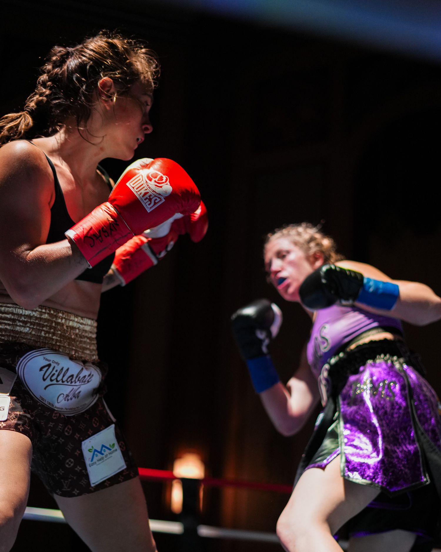 Female boxers exchanging punches in a competitive match with dramatic lighting.