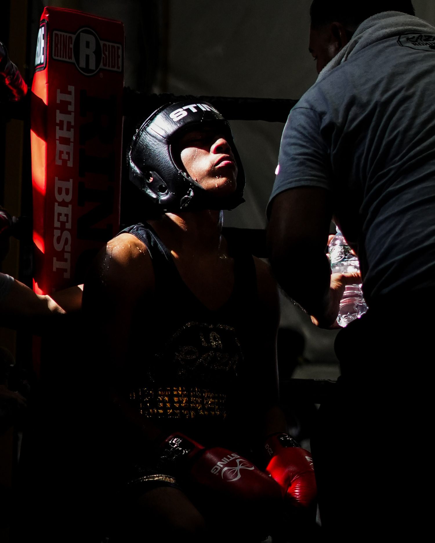 Boxer in protective headgear rests between rounds while receiving guidance from their corner.
