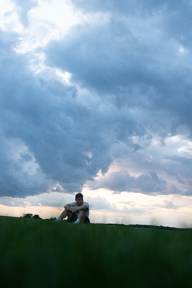 Silhouettes against dramatic cloudy sky during sunset on grassy horizon.