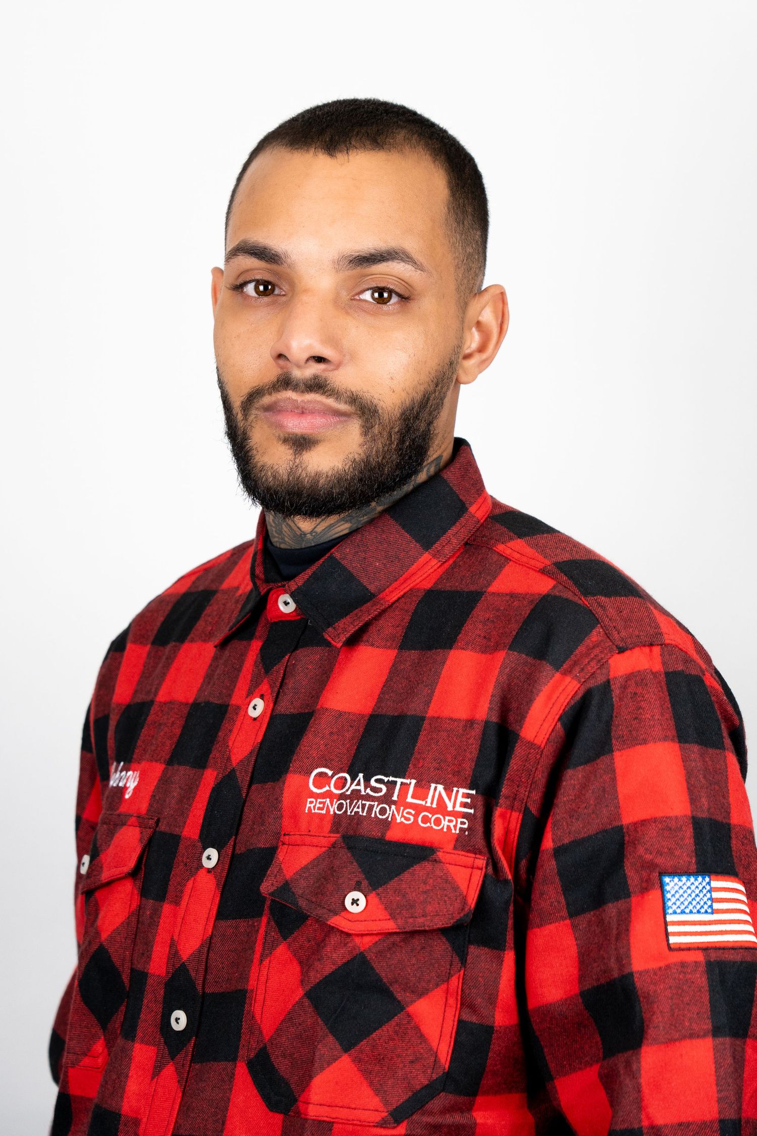 Man in red plaid flannel shirt with Coastline Renovations Corp logo and American flag patch.
