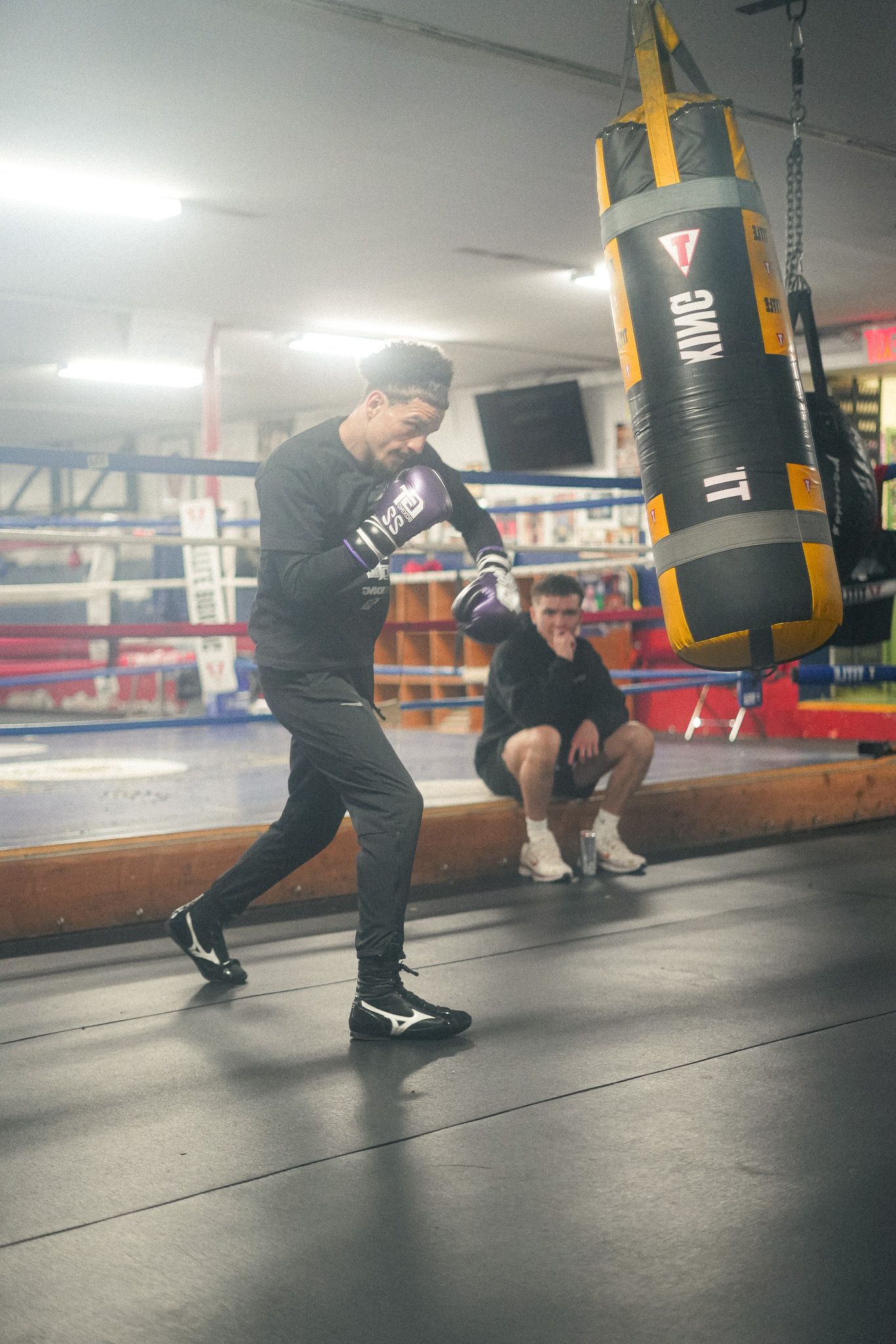 Athletes train with punching bags in a professional boxing gym setting.