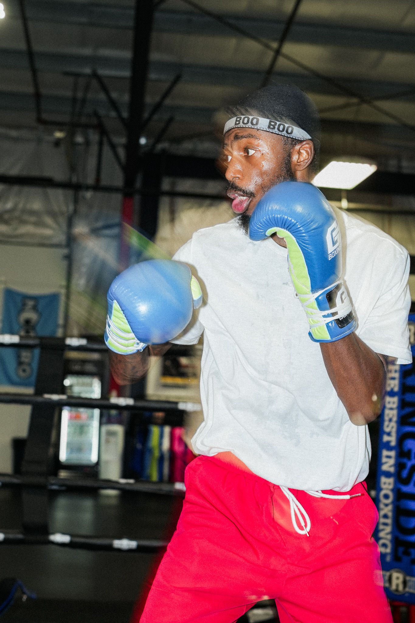 Boxer training with blue gloves and white shirt in a gym environment.