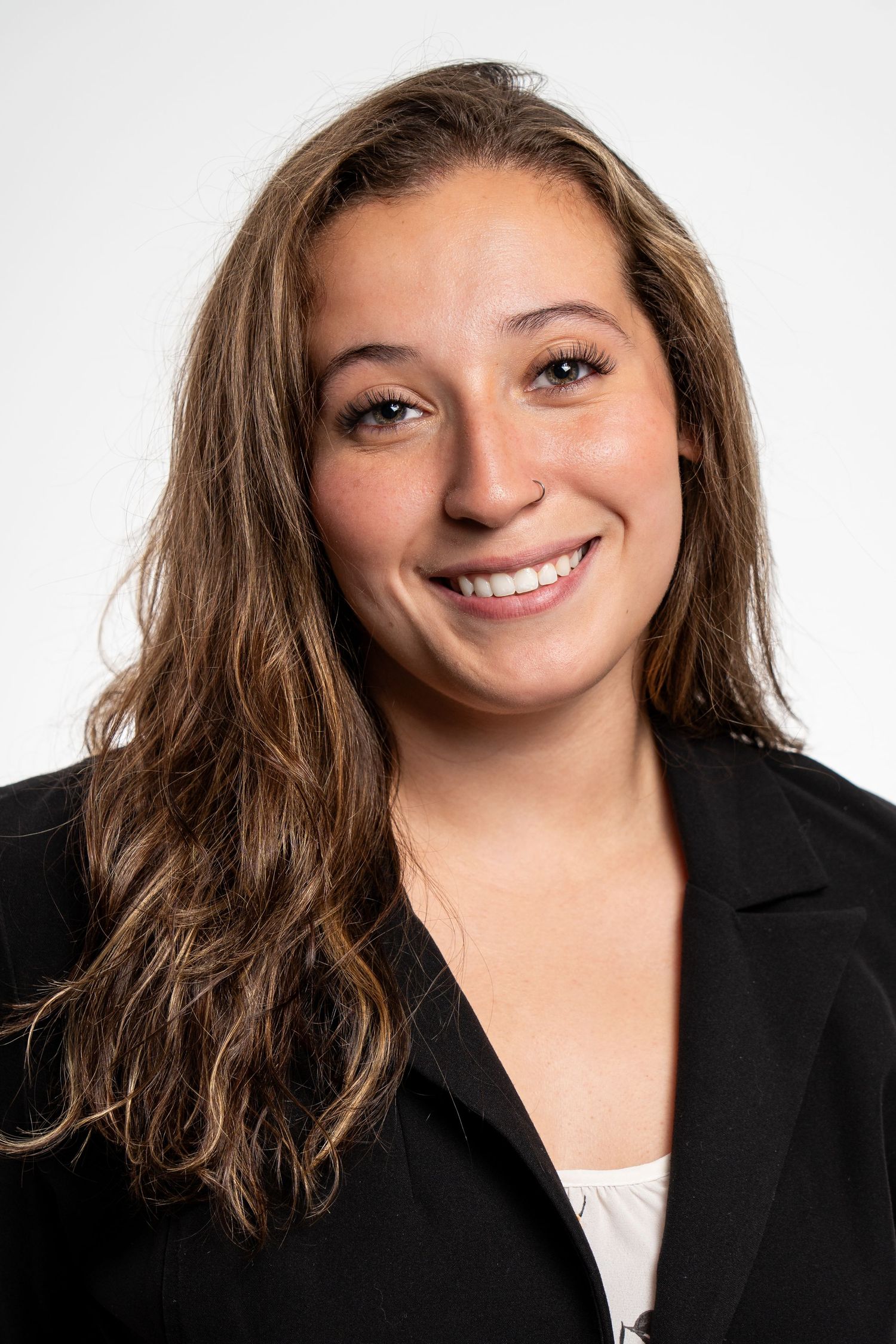 Young professional woman with long brown hair smiling in a black blazer against a white background.