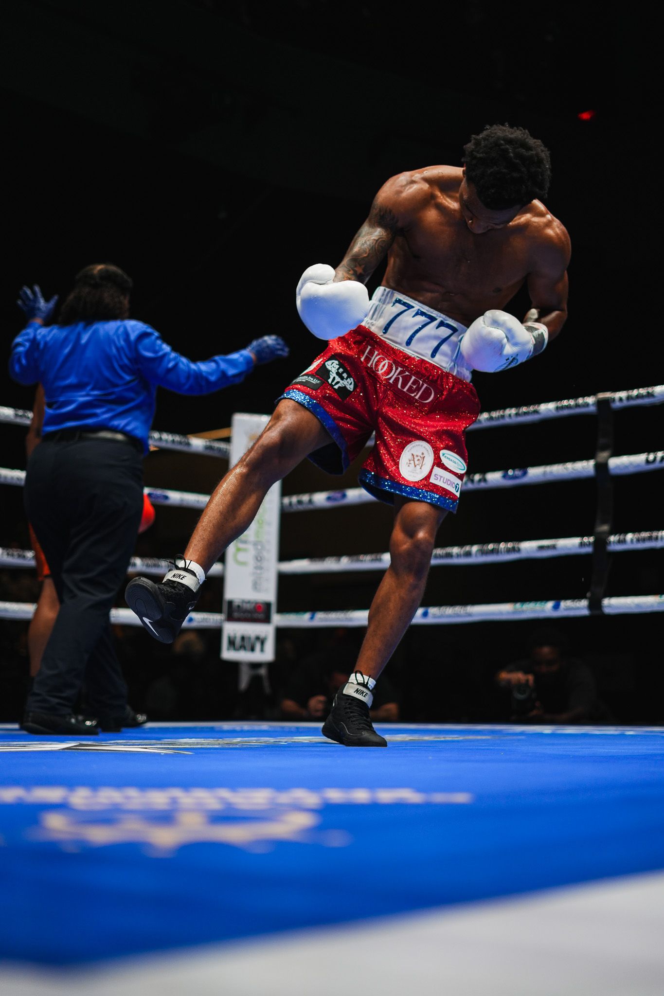 Boxer performs dynamic kick during professional match on blue canvas ring.