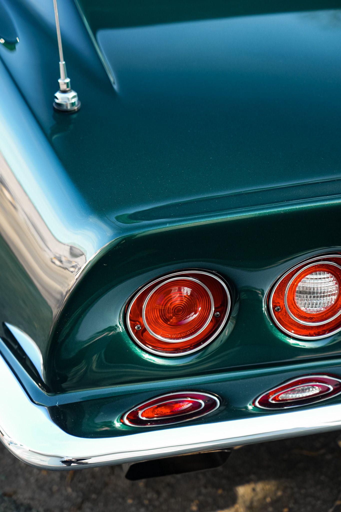 Classic car tail lights showing round red brake lights and chrome trim on a teal colored vehicle.