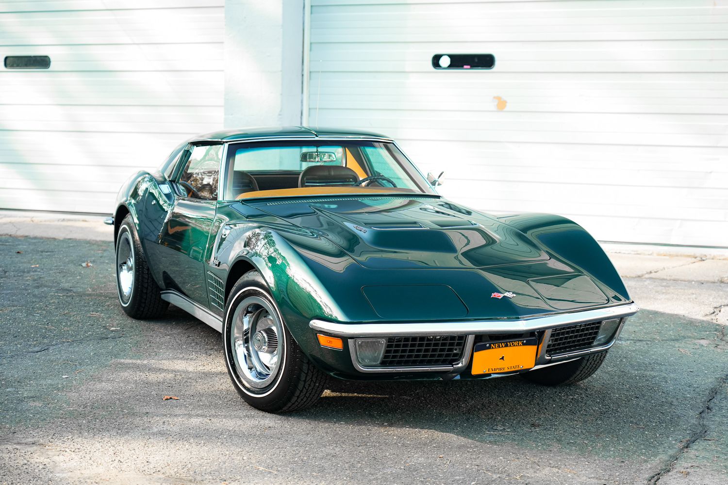 Classic green Chevrolet Corvette Stingray parked in front of garage doors.