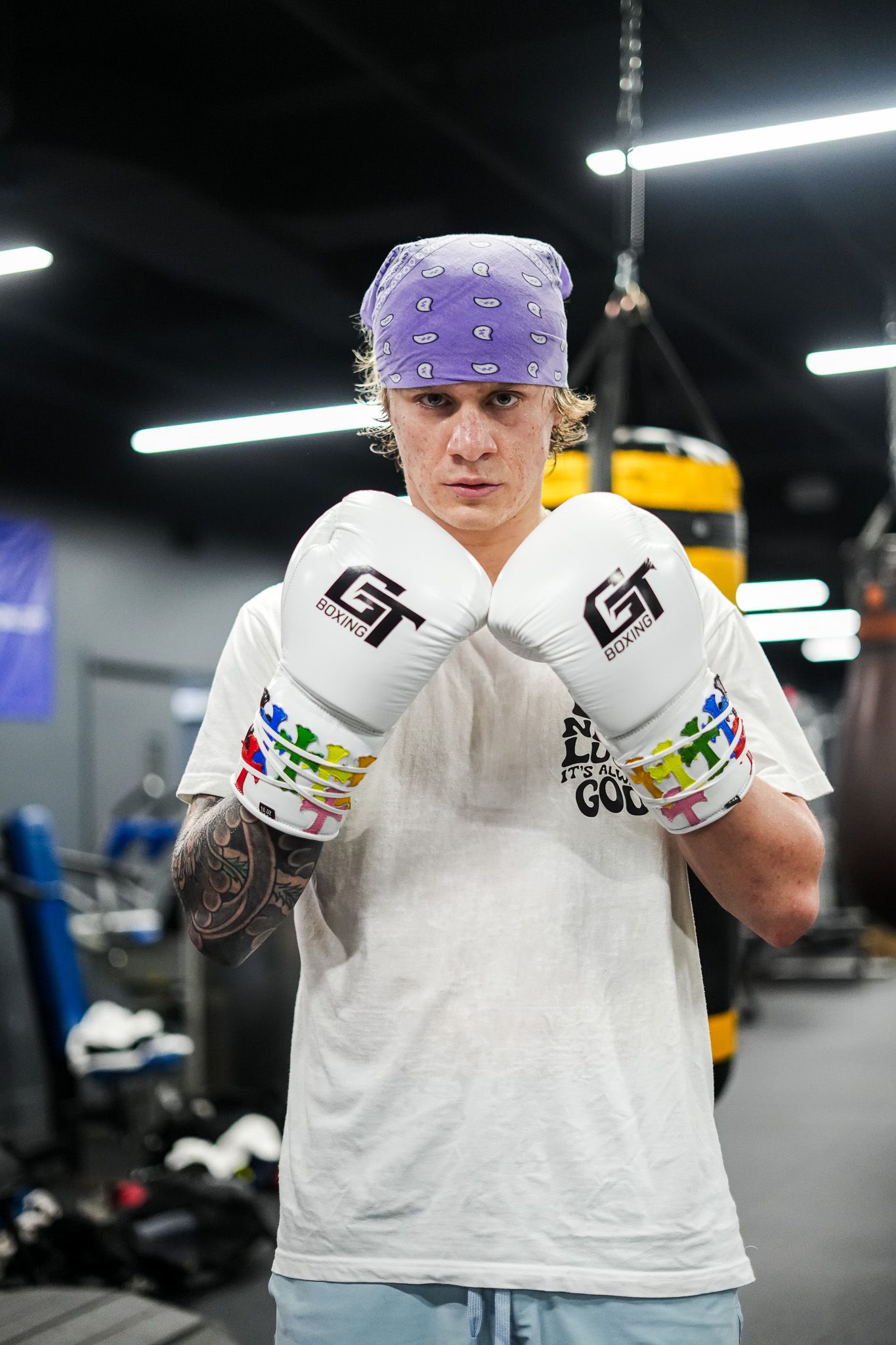 Boxing gloves and gear shown up close in a gym setting with purple headgear.