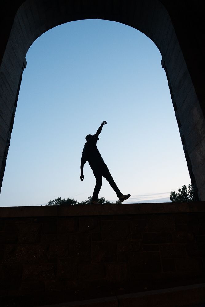 Silhouettes of people walking through an arched tunnel against bright sky background.