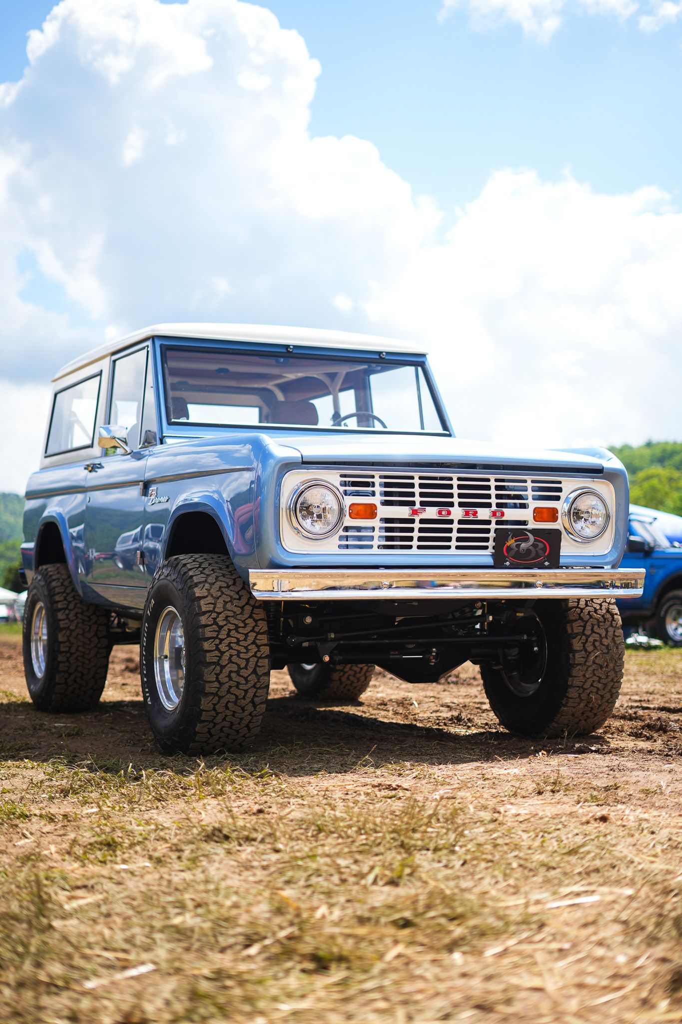 Row of vintage Ford Broncos lined up on dirt terrain against blue sky.