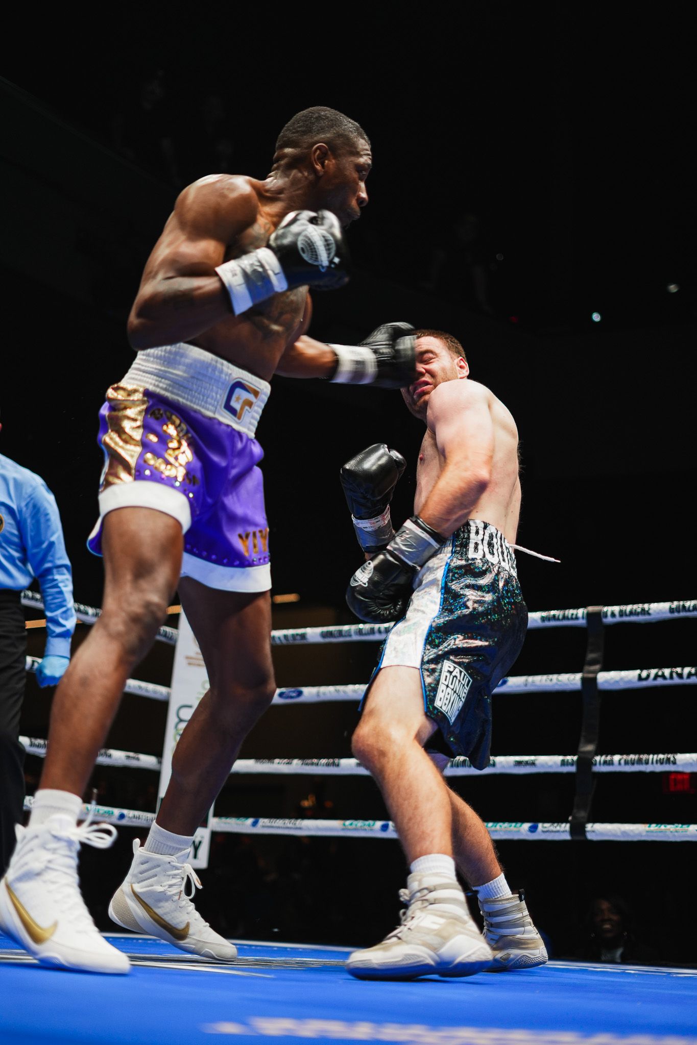 Boxers in white and purple trunks exchange punches during a competitive match.