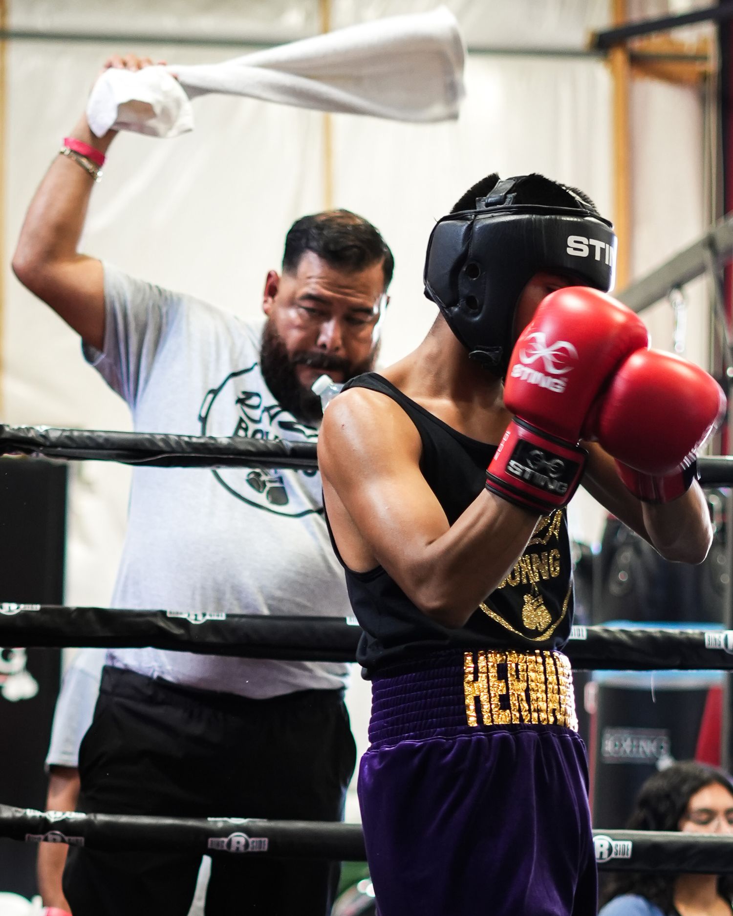 Boxing coach holds training pads while working with boxer during sparring session.