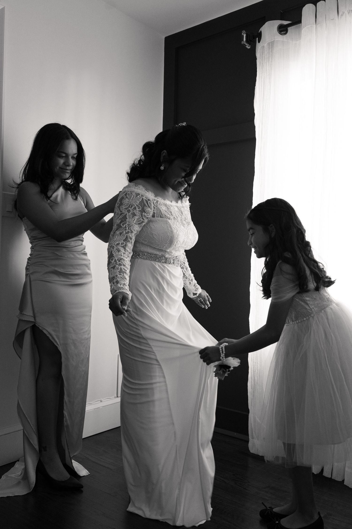 Wedding preparation scene with flowing white gowns and helping hands in black and white.