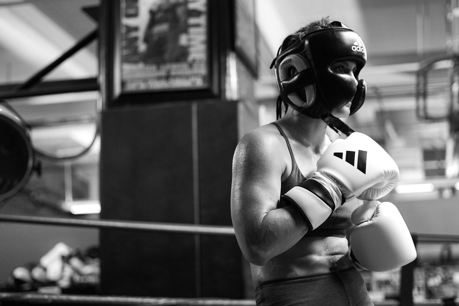Boxer in protective headgear and gloves stands ready in black and white composition.